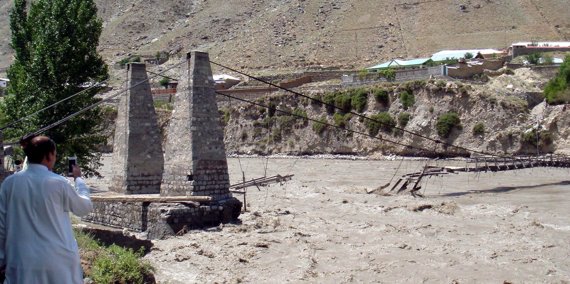 epa04854985 A picture made available on 21 July 2015 of a bridge over the Chitral river that was washed away by flash floods in the Darosh district of Chitral, Pakistan, on 20 July 2015. Six members of one family were among a dozen people killed by flash floods triggered by heavy monsoon rains across Pakistan, officials said on 20 July, warning of more thundershowers in the coming days. Raging water washed away a house in Chitral district of the north-western province of Khyber-Pakhtunkhwa, killing three people, provincial Information Minister Mushtaq Ghani said.  EPA/HAMMAD KHAN FAROOQI