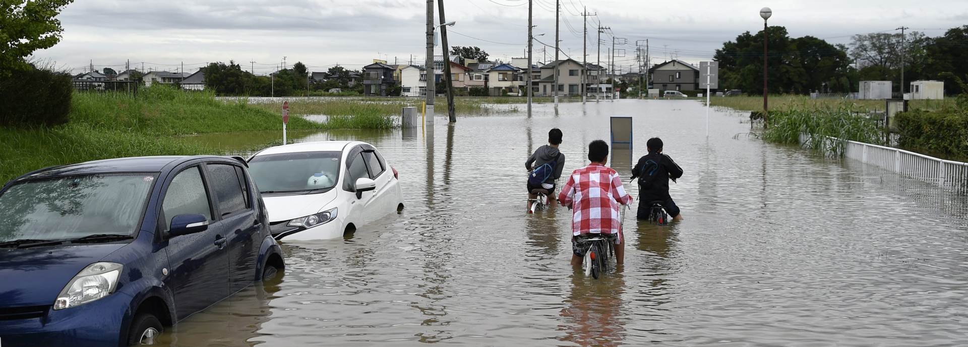 epa04923297 Young boys sit of their bicycles in a street flooded due to heavy rain generated by typhoon Etau in a residential area of Koshigaya, Saitama prefecture, north of Tokyo, Japan, 10 September 2015. According to local media reports, one person was feared dead and another missing and some 150,000 residents were ordered to evacuate their homes as flooding and mudslides hit eastern Japan. The Japan Meteorological Agency was warning of further mudslides and swollen rivers in eastern and north-eastern Japan with heavy rain pounding the region even after Typhoon Etau weakened into an extratropical depression.  EPA/FRANCK ROBICHON