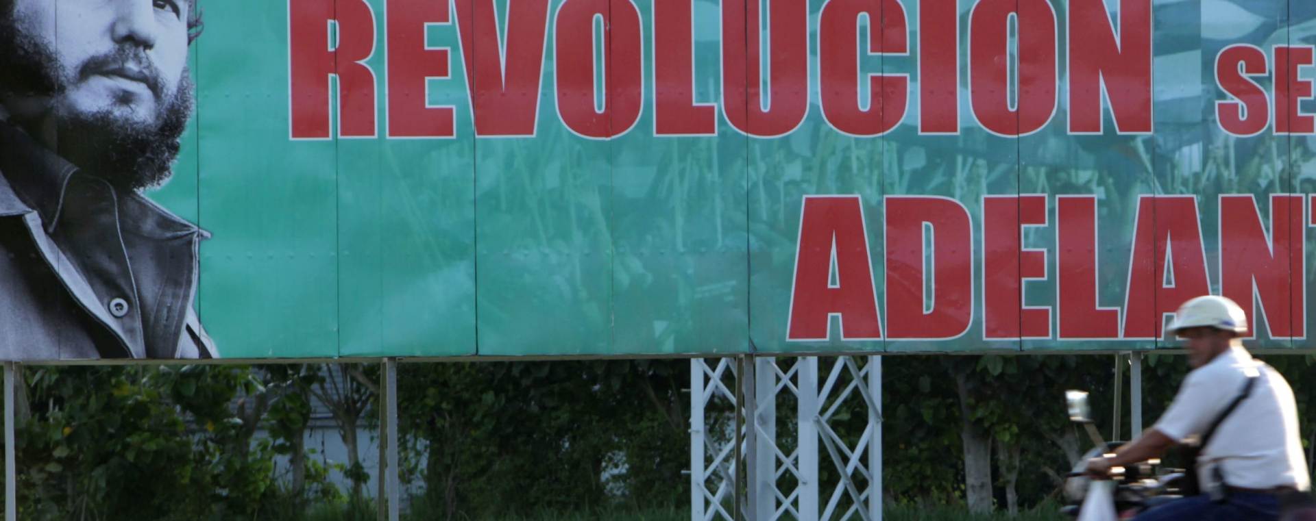 epa04882408 A motorcyclists drives past an image with the face of the leader of Cuban Revolution Fidel Castro Havana, Cuba, 13 August 2015. Today is Fidel Castro's 88th birthday. The placard reads 'The revolution will go on'.  EPA/ERNESTO MASTRASCUSA