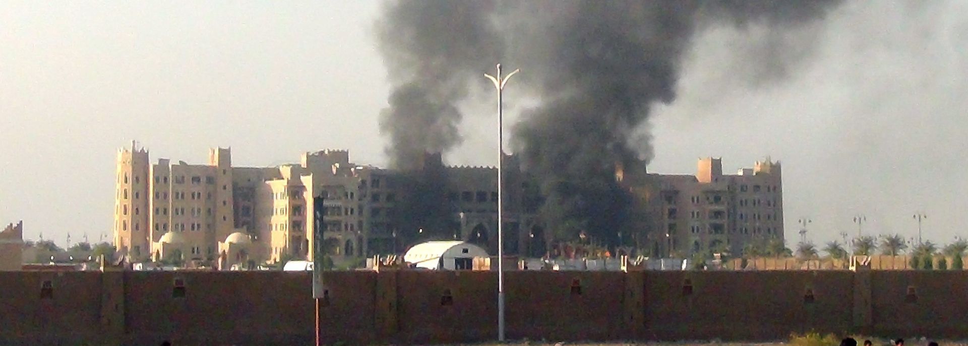 epa04965152 Yemenis gather near the Al-Qasr Hotel as columns of smoke rise after it was hit by rockets, in the southern port city of Aden, Yemen, 06 October 2015. According to reports, a hotel in Yemen's second city of Aden where Prime Minister Khaled Bahah and members of the government are using as residence, is on fire after being hit by three rockets. Bahah was not hurt by the attack.  EPA/STRINGER