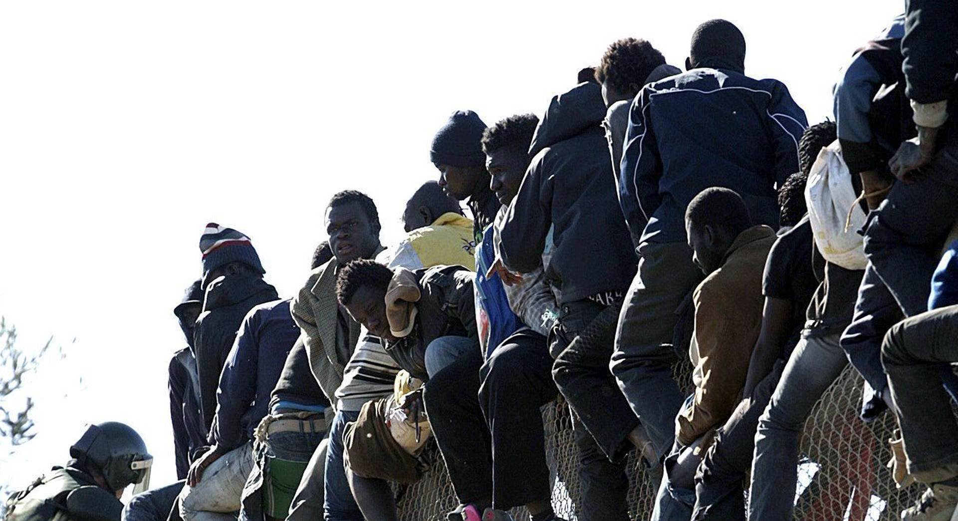 epa05035922 Migrants sit on the fence at the border between Morocco and Melilla, Spanish enclave on the north of Africa, as they try to enter the country, on 21 November 2015.  EPA/F. G GUERRERO