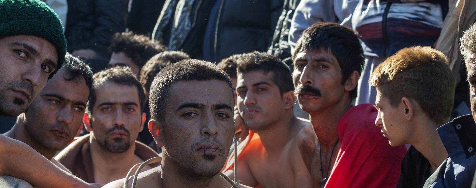 epa05038309 Several migrants, with stitched mouths in a sign of protest, sit in front of police cordon after they were barred from crossing the border, near Gevegelija, The Former Yugoslav Republic of Macedonia, 23 November 2015. Macedonia, Serbia, Croatia and Slovenia on 19 November stopped entry to all economic migrants, allowing only refugees from war-torn Syria, Iraq and Afghanistan to pass. Migrants barred from crossing the border line have been protesting for four days.  EPA/GEORGI LICOVSKI