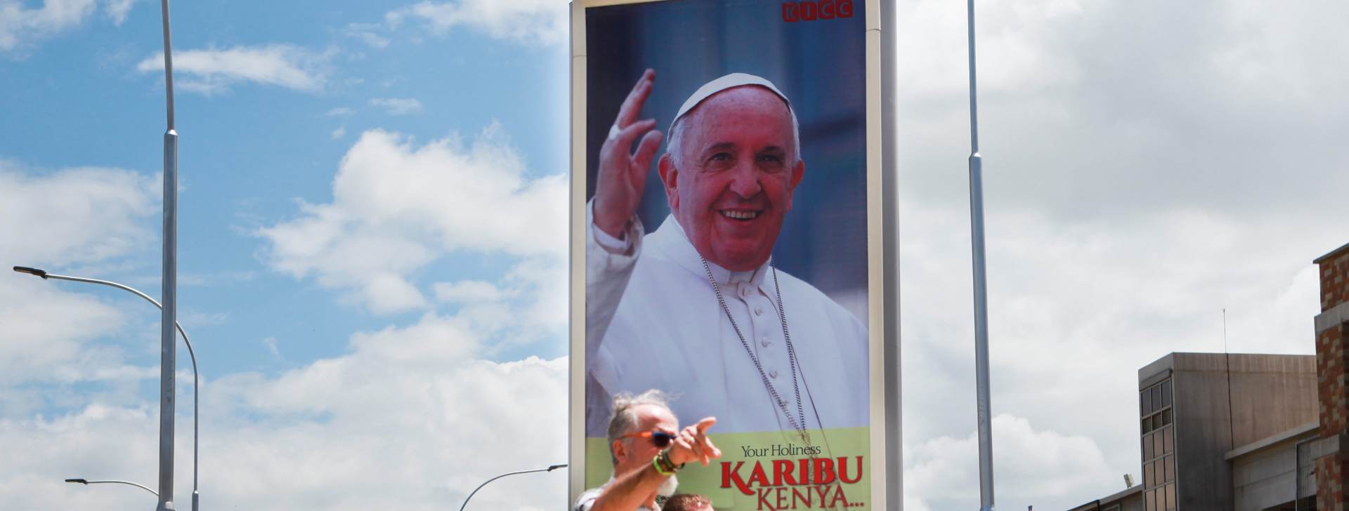 epa05038563 Tourists walk past a billboard welcoming Pope Francis to the country at the Jomo Kenyatta International Airport (JKIA), in Nairobi, Kenya, 23 November 2015. The Kenyan police says it has stepped up the security ahead of the upcoming papal visit that begins later this week while urging public to stay vigilant, in the wake of terror attacks in France and Mali by Islamist groups. Pope Francis is scheduled to arrive in Kenya on 25 November, his first stop on a three-nation Africa tour.  EPA/DANIEL IRUNGU