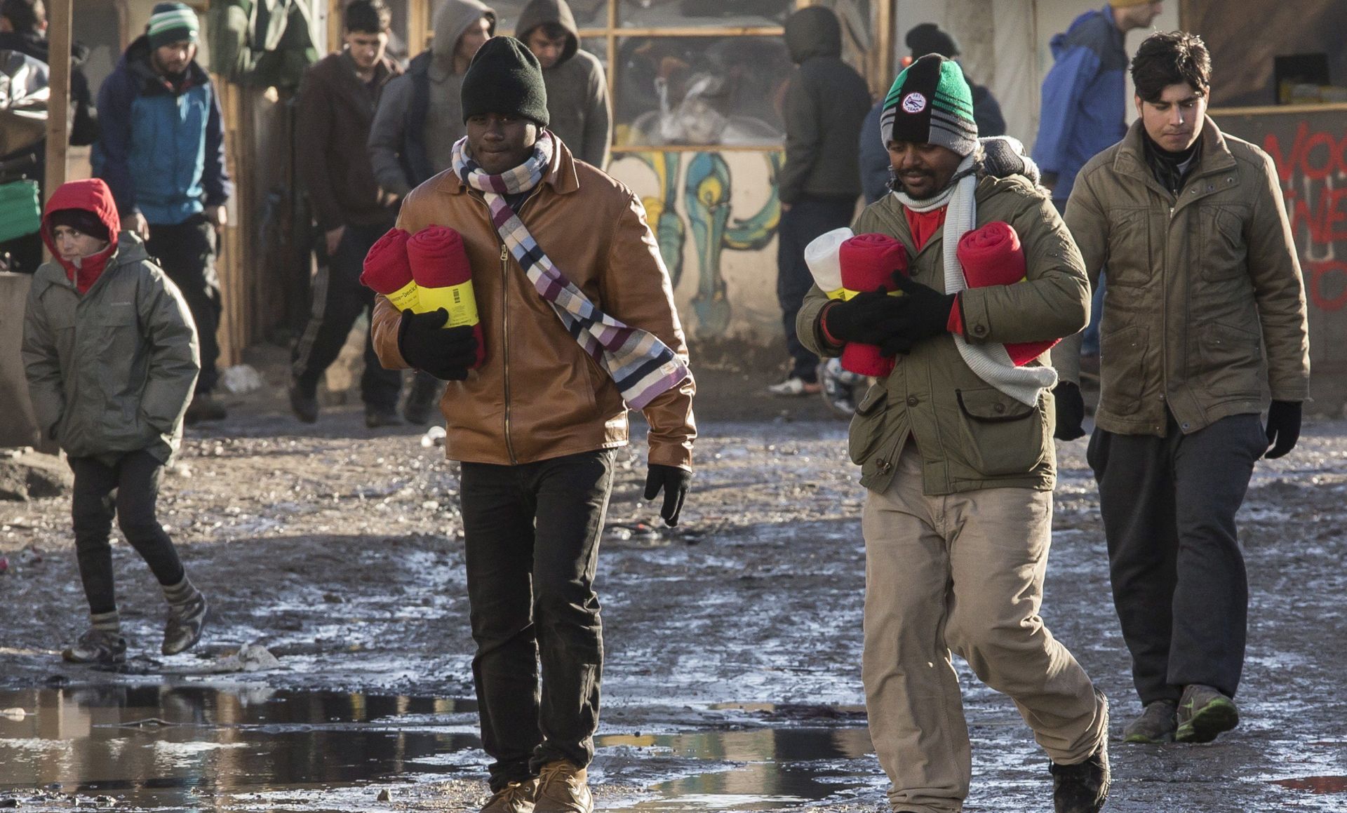 epa05162405 Migrants come back with warm covers to the tents and huts of the makeshift camp called 'The Jungle' next to the fenced area made of containers recycled in rooms in Calais, France, 15 February 2016. A new deadline was set by the French administration for the removal of migrant settlements in a week's time, as authorities plan to create a no-man zone in order to better spot migrants trying to access trucks and reach Britain. Between 4,000 and 7,000 migrants currently live in 'The Jungle'.  EPA/JULIEN WARNAND