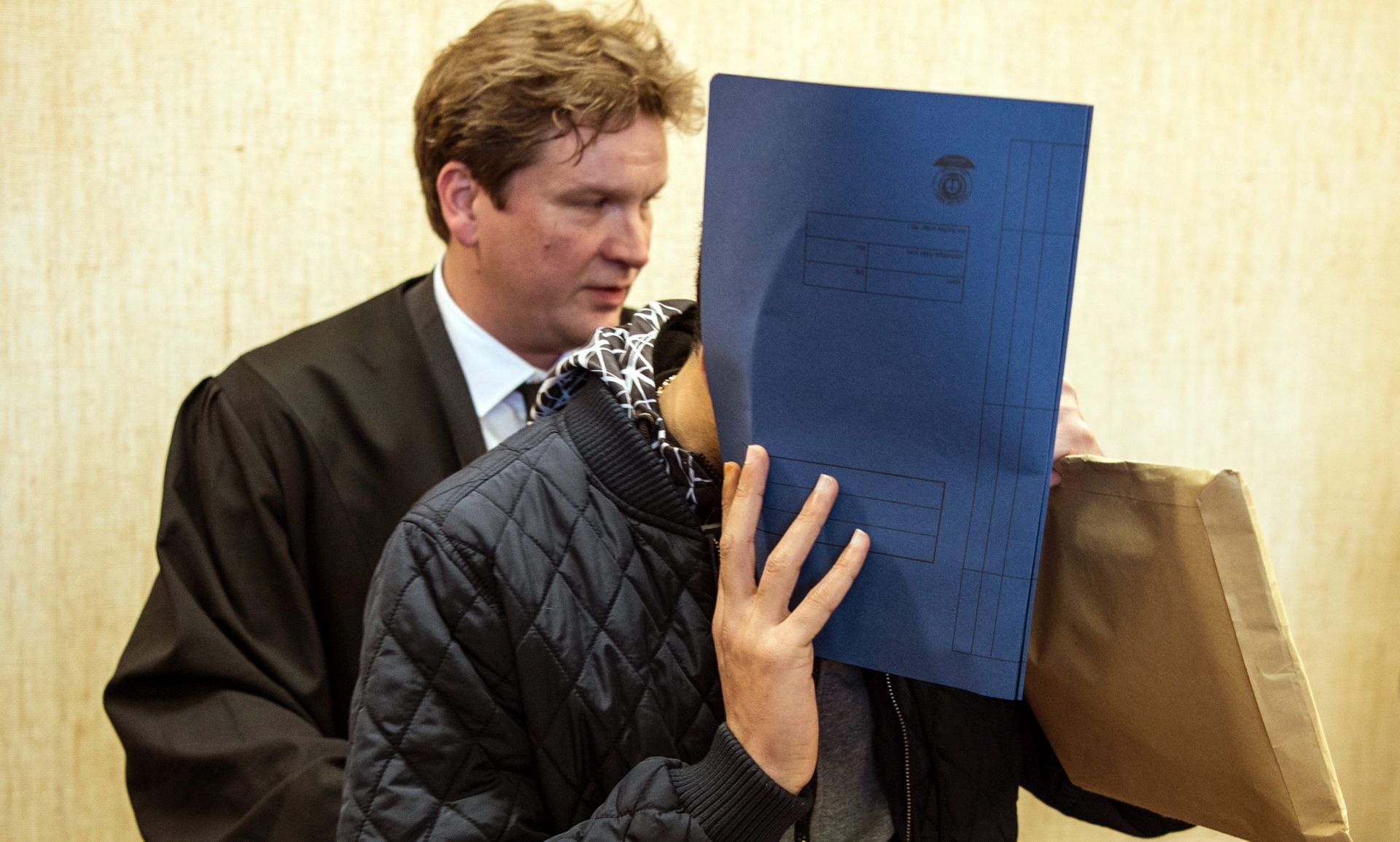 epa05177922 A defendant holds a file folder in front his face next to his lawyer Florian Storz (L) in the court room in Cologne, Germany, 24 February 2016. Three men who are charged with theft will appear before a German court in connection with a series of robberies and sexual assaults in Cologne during New Year's Eve celebration.  EPA/FEDERICO GAMBARINI