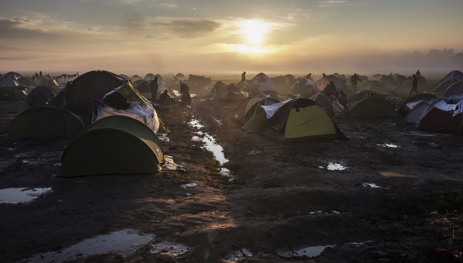 epa05205743 The sun rises as refugees stand around open fires waiting to cross the Greek-Macedonian border near Idomeni, northern Greece, 11 March 2016. Greece has registered in its territory some 36,000 migrants trapped due to entry restrictions already imposed by Macedonia in recent months, by denying entry to all those who are considered economic migrants, prohibiting the passage of Afghans, and finally denying entry to all Syrians and Iraqis who are not from combat areas.  EPA/VALDRIN XHEMAJ