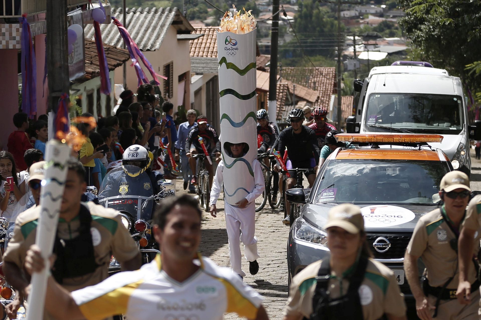 epa05289942 A handout picture provided by the Rio Olympics 2016 organization committee shows a man dressed up as the Olympic flame (C) as the Olympic torch (front L) passes through Corumba de Goias, Brazil, 04 May 2016. The Olympic flame has started its tour of Brazil, which will end on 05 August 2016 with the opening of the Olympic Games at the Maracana stadium, in Rio de Janeiro  EPA/FERNANDO SOUTELLO / HANDOUT  HANDOUT EDITORIAL USE ONLY/NO SALES