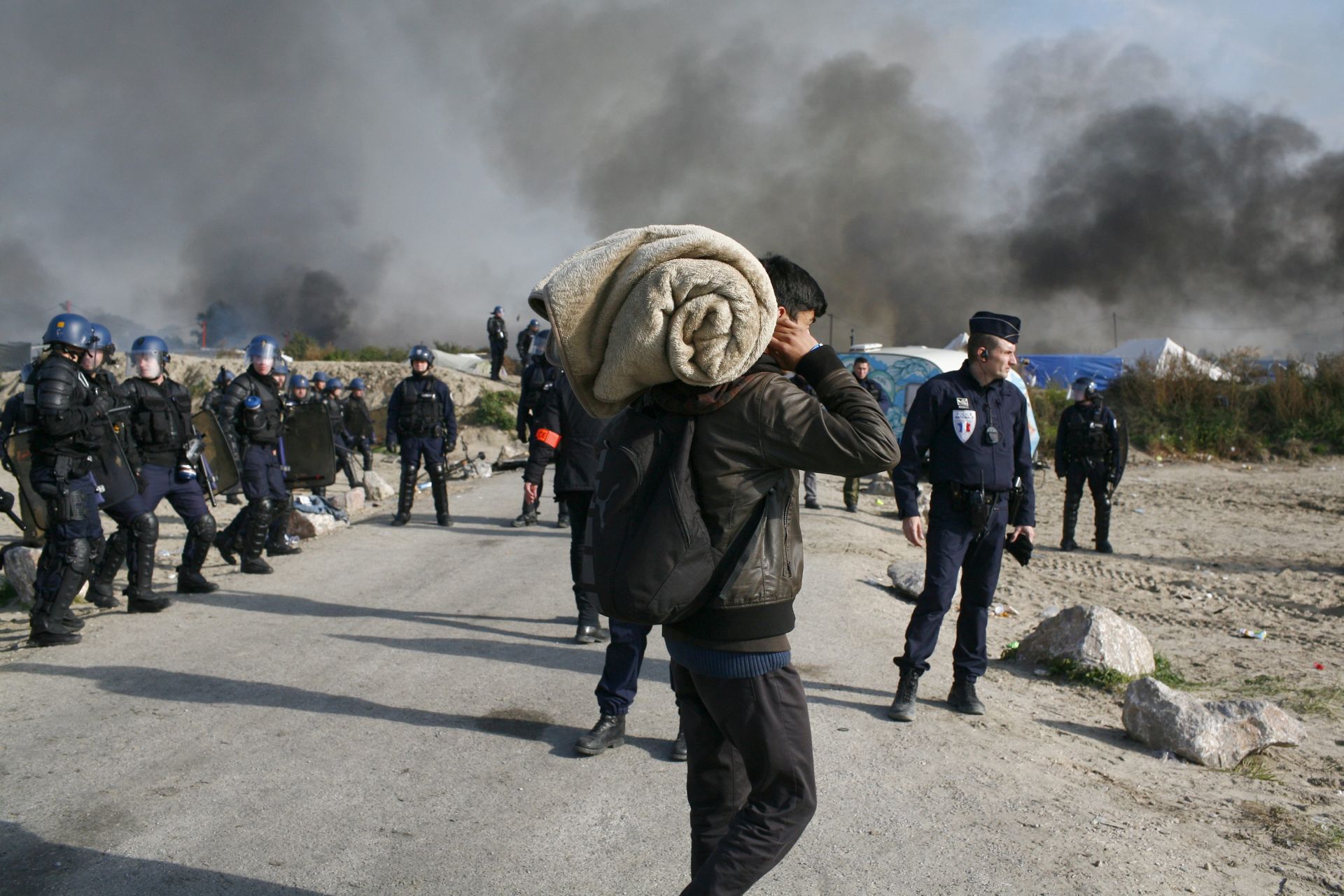 epa05603735 Migrants and French police during the evacuation of the 'Jungle' refugee camp in Calais, France, early 26 October 2016. French authorities continued to clear the makeshift camp for a third day, with refugees being deported to accommodation centers across the country.  EPA/THIBAULT VANDERMERSCH