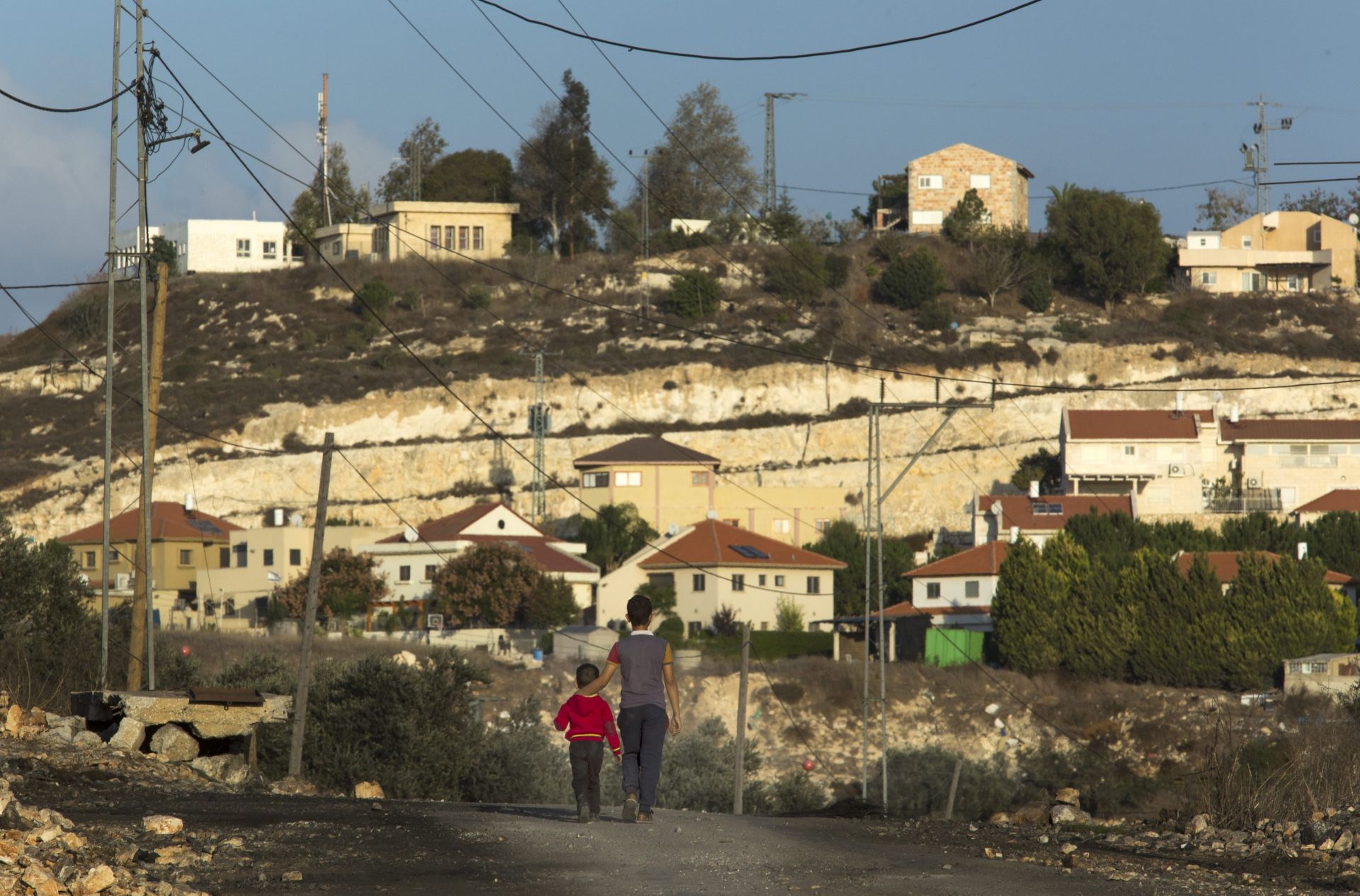 epa05636257 A picture made available on 18 November 2016 shows the Jewish settlement of Kedumim in the West Bank, as it is seen from the Palestinian village of Qaddum, 17 November 2016, as Palestinian children walk on a road closed by the Israeli army that in the past linked the two residential areas. The Israeli army issued an alert to settlers in Kedumim to remain indoors and to lock their doors due to a possible 'terrorist' infiltration. The Israeli security forces are said to be investigating the threat with no further details immediately available. Qaddum has been the scene of almost weekly stone-throwing clashes between Palestinian youths and Israeli security forces over the confiscation of Palestinian lands.  EPA/JIM HOLLANDER