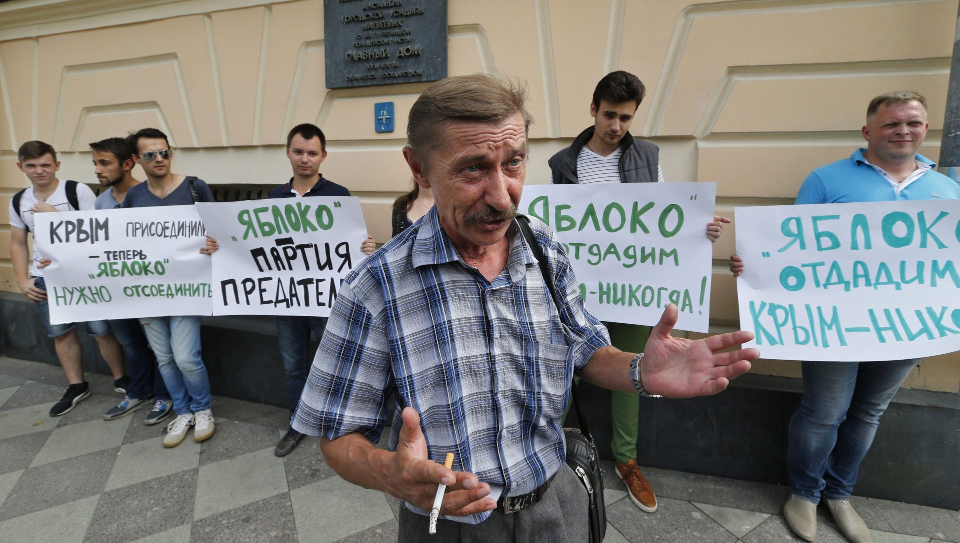epa05498953 A man guestures in front of the row of the Young Guard of the United Russia movement members holding posters (L-R): 'The Crimea - reunited, now Apple should be excluded', 'Yabloko is party of traitors' and 'We will give up Apple, never - the Crimea ' during a rally in front of Yabloko (Apple) political party office in Moscow, Russia 19 August 2016. Young Guard of the United Russia movement demands to stop statements of illegality of Crimea's reunion with Russia.  EPA/YURI KOCHETKOV