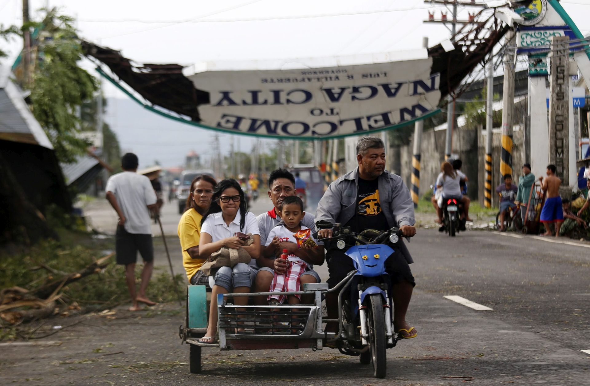 epa05688304 Filipino villagers ride a three wheeled motorcycle next to a toppled signboard in the typhoon-hit city of Naga, Camarines Sur, Philippines, 26 December 2016. According to Office of Civil Defense (OCD) report on 26 December, hundreds of thousands of villagers spent their Christmas day in evacuation centers in Bicol region, many flights were cancelled at Manila's international airport, and scores of sea vessels have reportedly sunk as Typhoon Nock-ten brought howling winds and strong rains in central Philippines.  EPA/FRANCIS R. MALASIG
