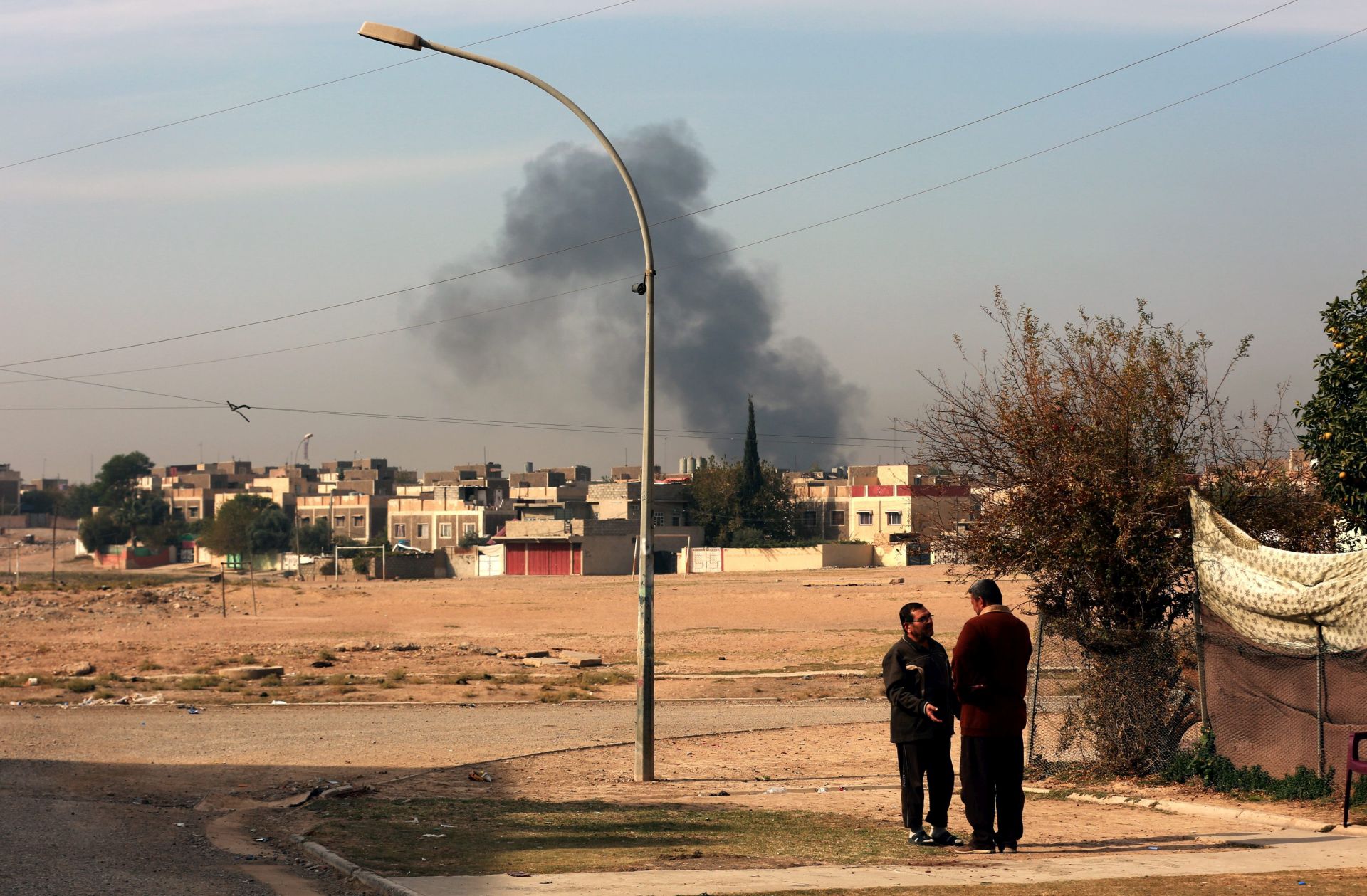 epa05649645 Two Iraqi men from Mosul talk with each other as the smoke rises from a location of heavy clashes between the Iraqi forces and Islamic state group, eastern Mosul, Iraq, 27 November 2016. Iraqi security forces recaptured two districts in Mosul as operations continue to liberate the city from Islamic State militants (IS), Iraqi officers said.  EPA/AHMED JALIL