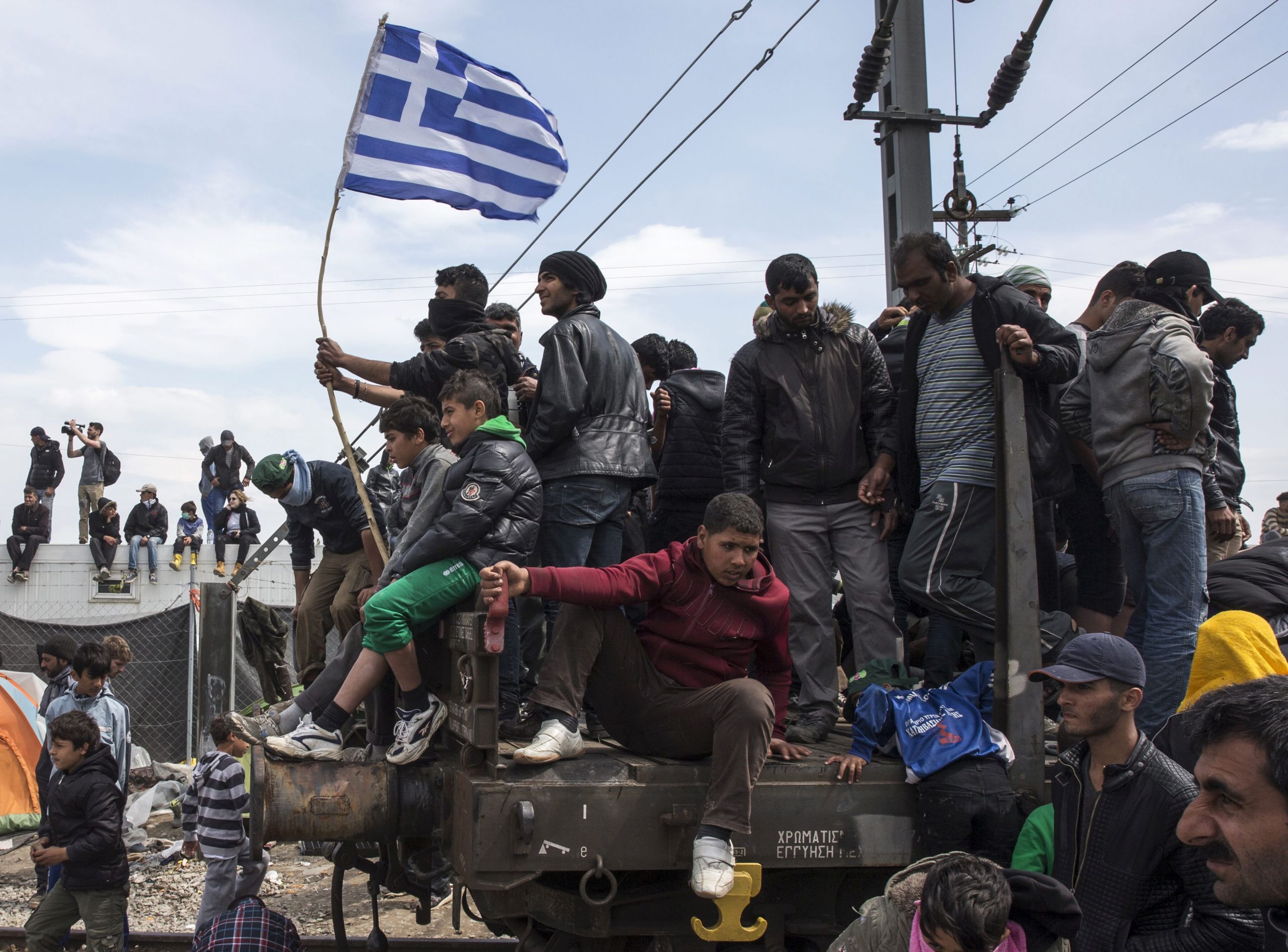 epa05254261 Migrants protest in a wagon waving a Greek national flag at a refugee camp near the Greek-FYROM border near the village of Idomeni, northern Greece, 11 April 2016. Thousands of refugees are stuck in Greece following the closure of the borders of the Balkan route and after the implementation of the migration agreement between the European Union (EU) and Turkey.  EPA/VALDRIN XHEMAJ