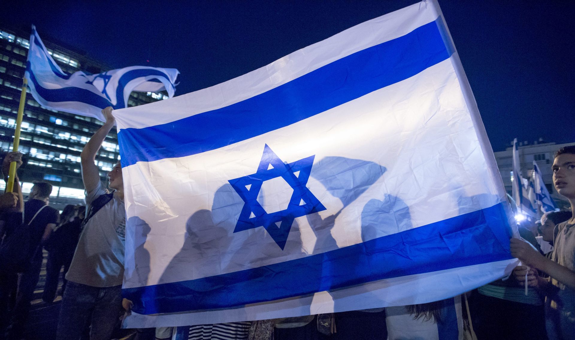 epa05267555 Israelis behind a large Israeli flag as they attend a right-wing rally in Tel Aviv, Israel, 19 April 2016 in support of an Israeli soldier indicted for manslaughter in the killing of a Palestinian. The Israeli soldier, Elor Azaria, age 19, was charged on 18 April in court with manslaughter and 'violation of the rules of engagement' in the shooting of a Palestinian Abdel Fattah al-Sharif as he lay wounded on the ground in Hebron on 24 March 2016. Azaria shot al-Sharif in the head with one bullet.  EPA/JIM HOLLANDER