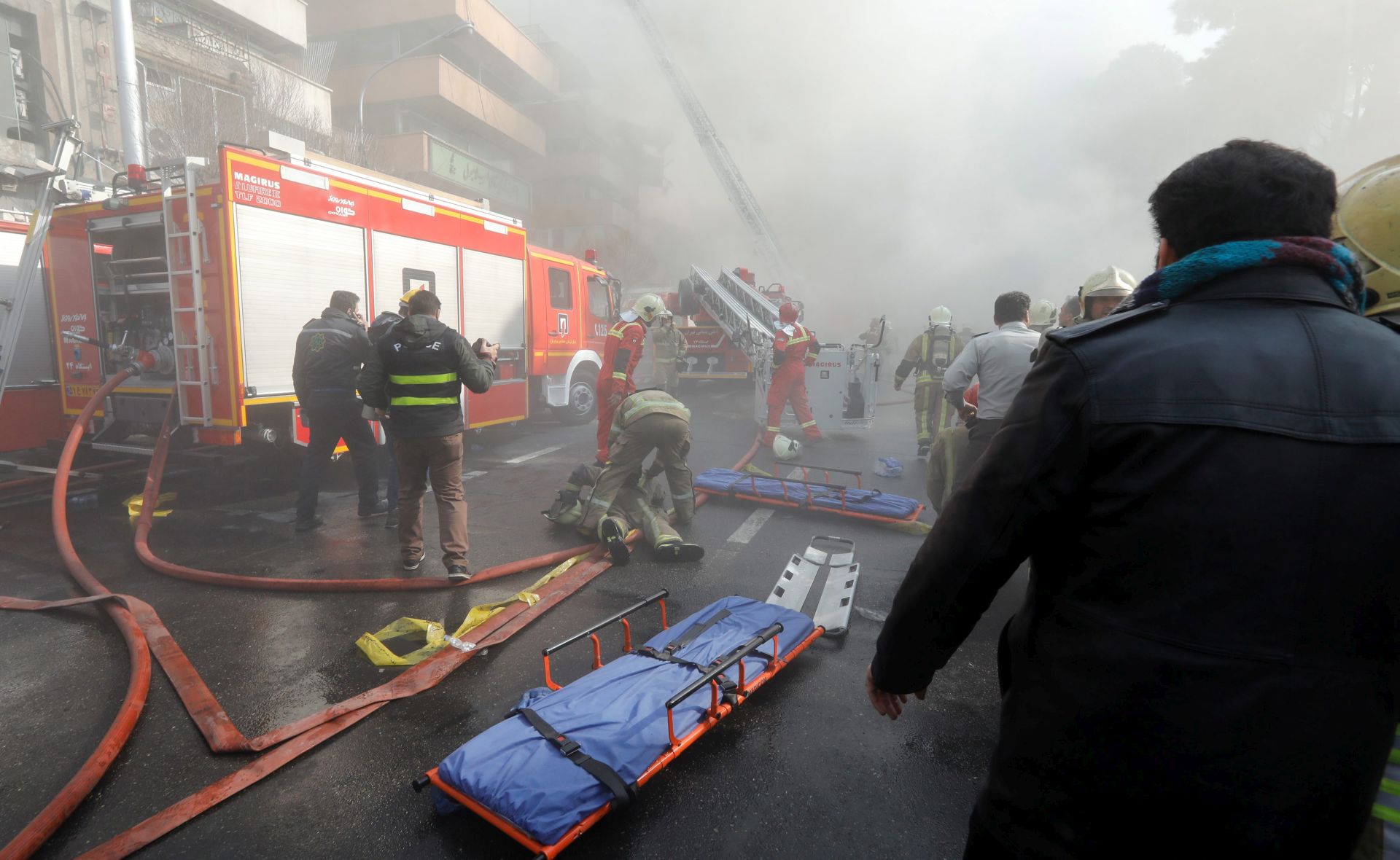 epa05730084 Iranian fire fighters prepare as the iconic Plasco building collapses after a fire in Tehran, Iran, 19 January 2017. Media reported that the major commercial building in Tehran has collapsed after hours of a severe fire, according to Iranian state media. At least 30 firefighters are believed to have died after being trapped on the upper floors of the building.  EPA/ABEDIN TAHERKENAREH