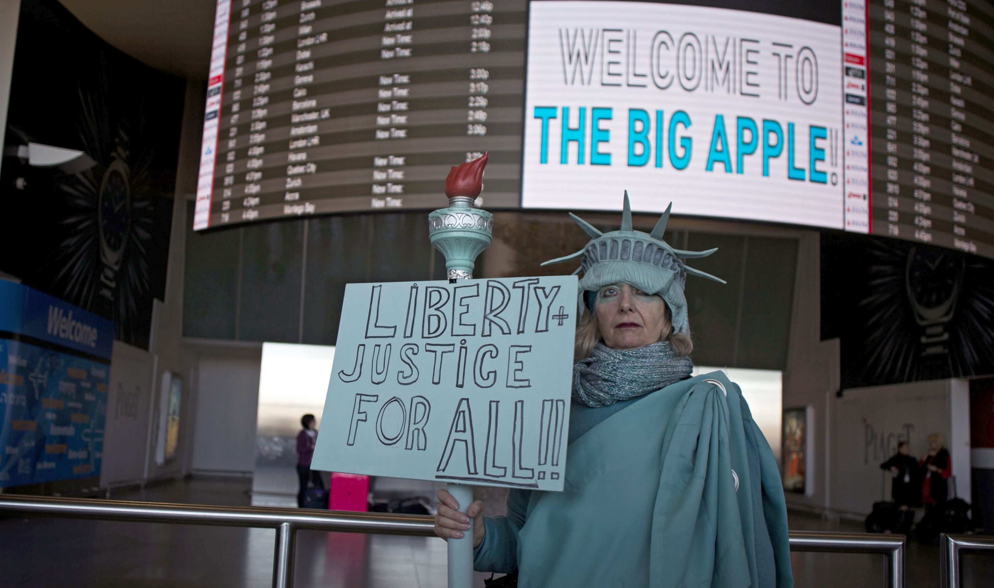 epa05771343 A woman dressed as the Statue of Liberty holds a placard 'Liberty and Justice for All' as she stands inside the arrivals section of Terminal 4 at John F. Kennedy International Airport in Queens, New York, USA, 04 February 2017. A federal judge on 03 February issued a temporary restraining order blocking enforcement of US President Trump's executive order from 27 January that banned people from seven mainly Muslim countries from entering the United States. The US Department of Homeland Security announced on 04 February it has suspended all actions to implement the immigration order and will resume standard inspections of travelers.  EPA/JOHN TAGGART