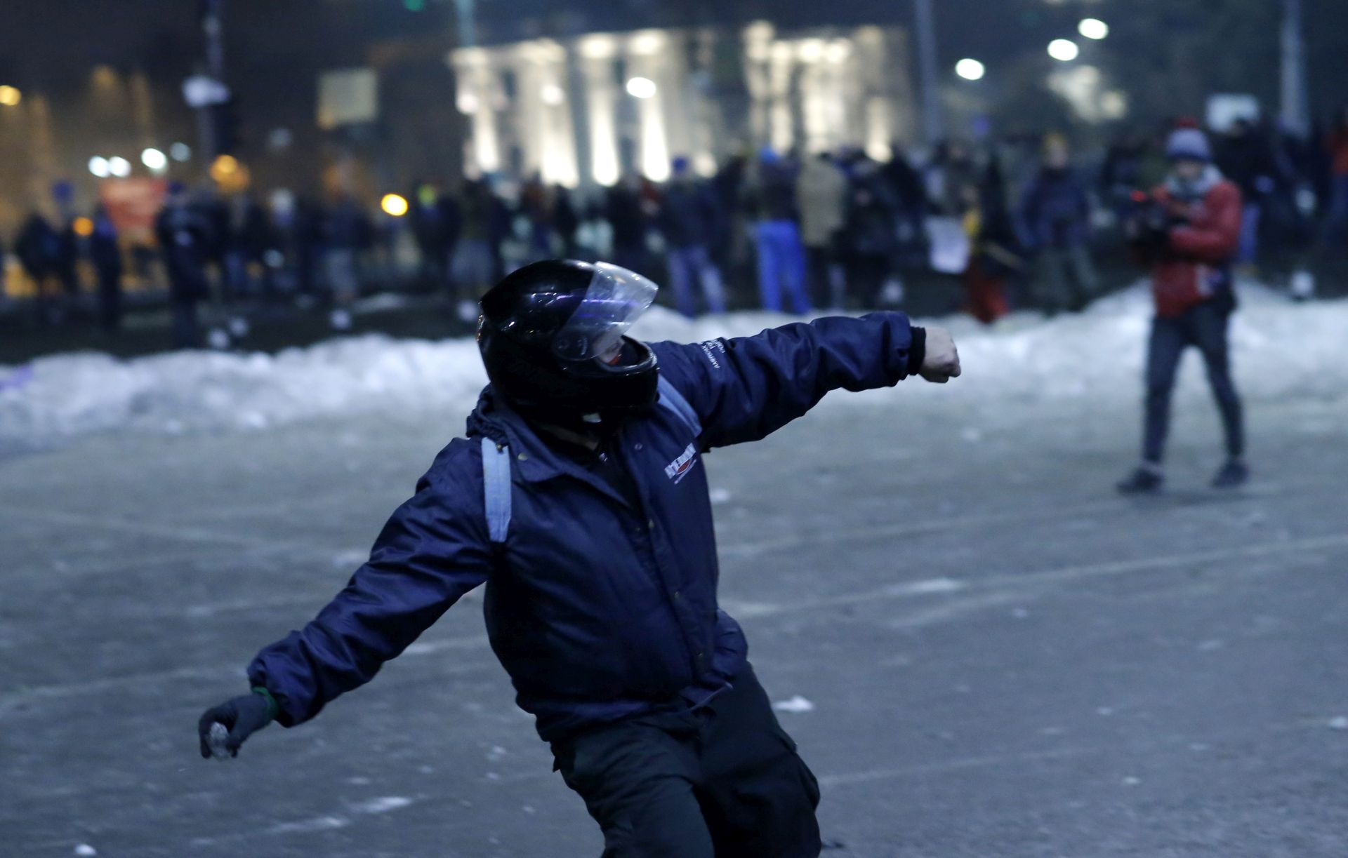 epa05765713 A protester wearing a motorcycle helmet throws an ice piece towards the riot police line during a protest rally in front of government headquarters in Bucharest, Romania, early 02 February 2017. Up to 100,000 people gathered peacefully in front of the government building and blocked the city traffic to protest against a government bill, that passed through during a government session on the evening of 31 January, as a government ordinance to pardon those sentenced to jail terms shorter than five years. According to media reports, the protests took a violent turn when a few hundred allegedly soccer supporters provoked riot police with stones, flares and firecrackers and the riot police responded with tear gas and arrests.  EPA/ROBERT GHEMENT