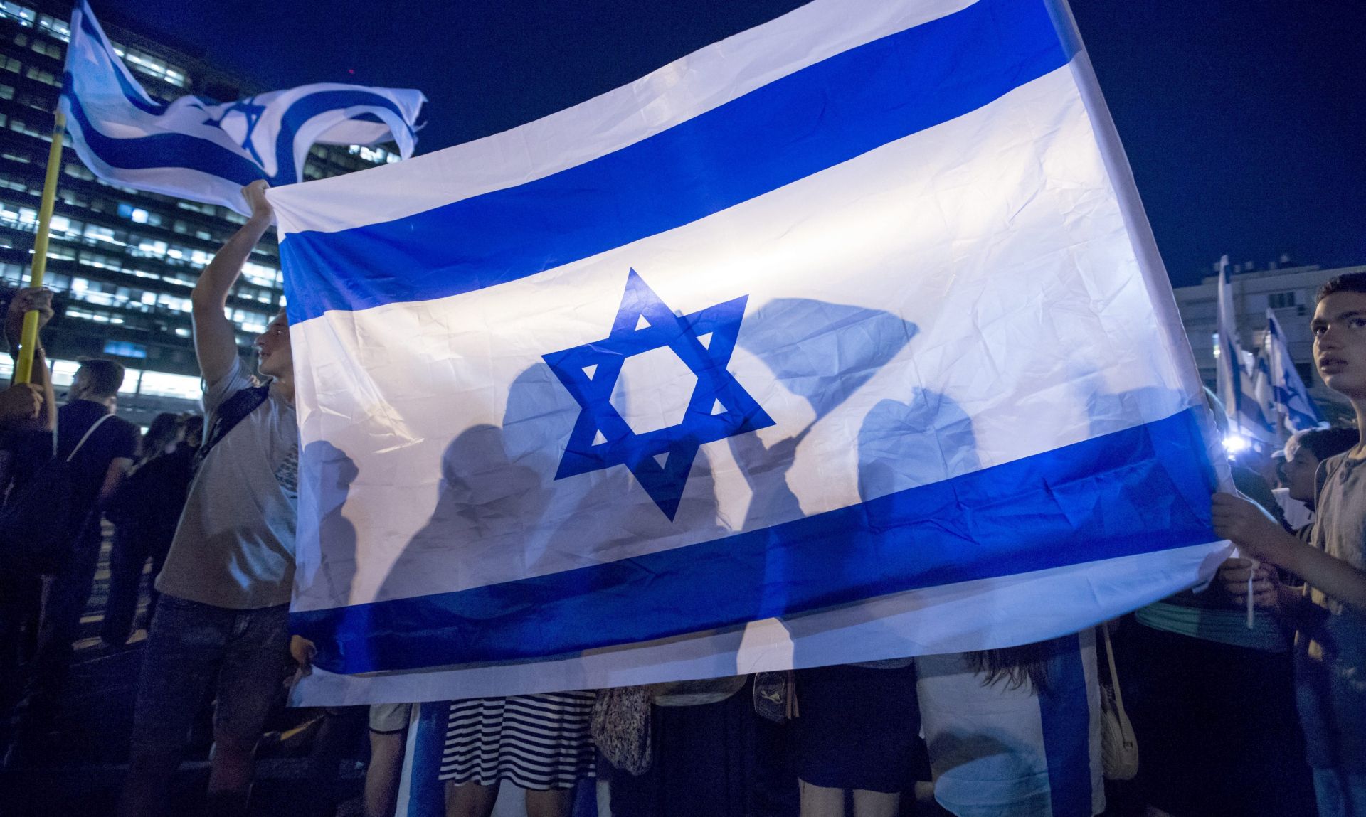epa05267555 Israelis behind a large Israeli flag as they attend a right-wing rally in Tel Aviv, Israel, 19 April 2016 in support of an Israeli soldier indicted for manslaughter in the killing of a Palestinian. The Israeli soldier, Elor Azaria, age 19, was charged on 18 April in court with manslaughter and 'violation of the rules of engagement' in the shooting of a Palestinian Abdel Fattah al-Sharif as he lay wounded on the ground in Hebron on 24 March 2016. Azaria shot al-Sharif in the head with one bullet.  EPA/JIM HOLLANDER