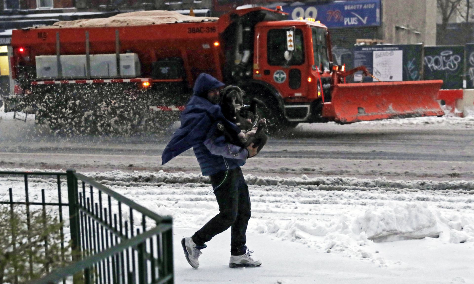 epa05847650 A man holds his dog as he walks through the snow past a New York City snow plow on the Lower East Side in New York City, New York, USA, 14 March 2017. While New York City and Boston had been issued a blizzard warning, that has been downgraded to a winter storm as the storm's track shifted resulting in a shift to rain for both cities and smaller forecast snowfall totals.  EPA/JASON SZENES