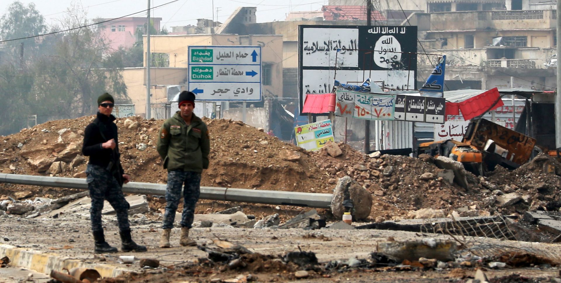 epaselect epa05860496 Iraqi policemen stand next a placard with the slogans of Islamic state group (IS) at a street in an area west of Mosul, Iraq, 20 March 2017. Iraqi forces backed by airstrikes from a US-led coalition recaptured many disricts in western Mosul, and the fighting has reached into the Old City and around the Mosul's al-Nuri Mosque, where the Islamic State (IS) group leader Abu Bakr al-Baghdadi had declared his 'caliphate' in his only known public appearance in 2014.  EPA/AHMED JALIL