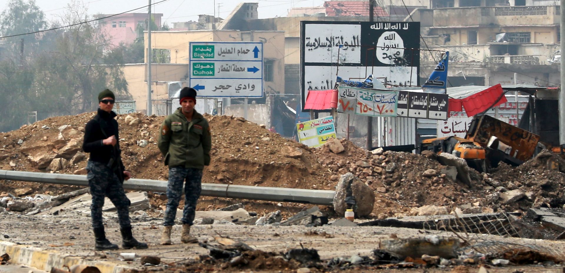 epaselect epa05860496 Iraqi policemen stand next a placard with the slogans of Islamic state group (IS) at a street in an area west of Mosul, Iraq, 20 March 2017. Iraqi forces backed by airstrikes from a US-led coalition recaptured many disricts in western Mosul, and the fighting has reached into the Old City and around the Mosul's al-Nuri Mosque, where the Islamic State (IS) group leader Abu Bakr al-Baghdadi had declared his 'caliphate' in his only known public appearance in 2014.  EPA/AHMED JALIL