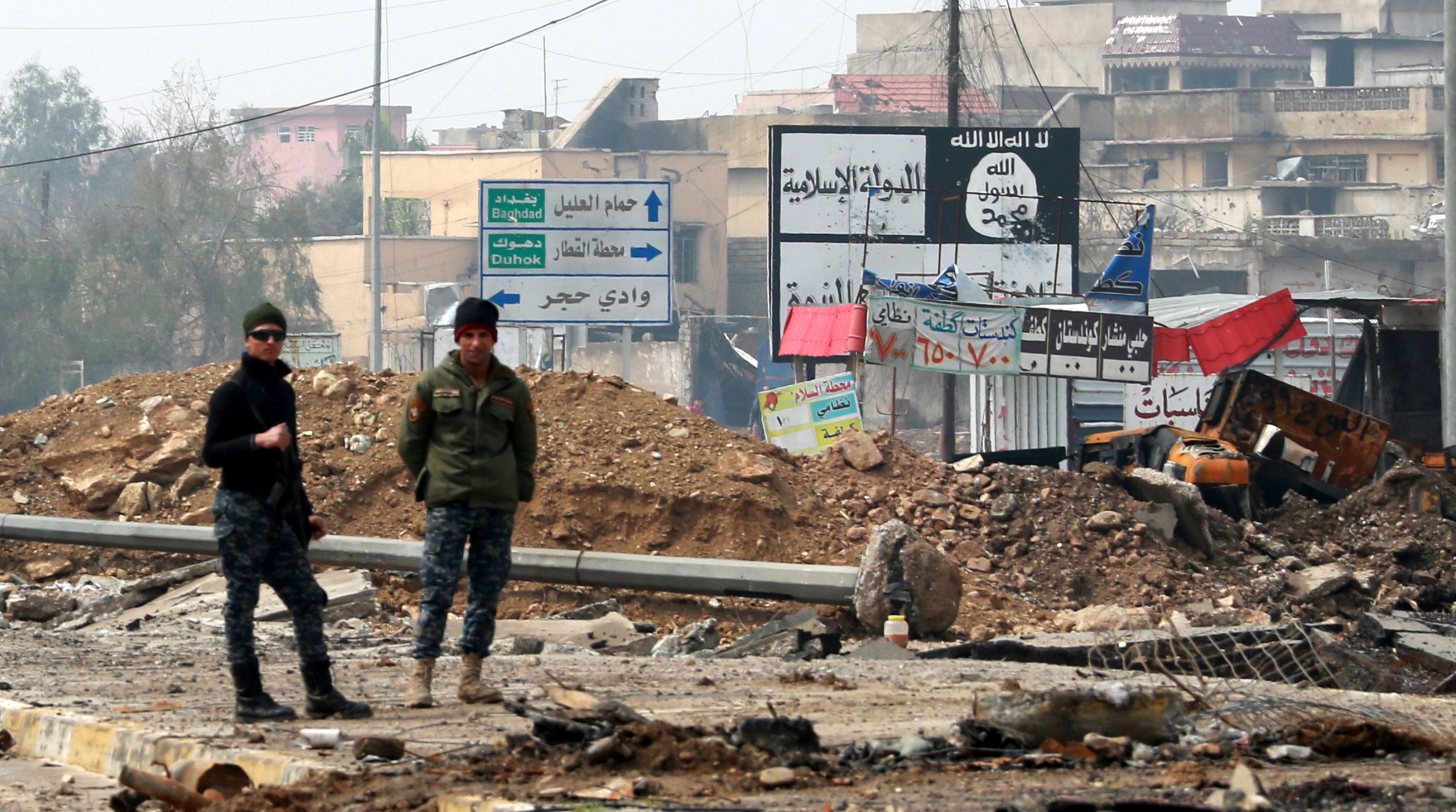 epaselect epa05860496 Iraqi policemen stand next a placard with the slogans of Islamic state group (IS) at a street in an area west of Mosul, Iraq, 20 March 2017. Iraqi forces backed by airstrikes from a US-led coalition recaptured many disricts in western Mosul, and the fighting has reached into the Old City and around the Mosul's al-Nuri Mosque, where the Islamic State (IS) group leader Abu Bakr al-Baghdadi had declared his 'caliphate' in his only known public appearance in 2014.  EPA/AHMED JALIL
