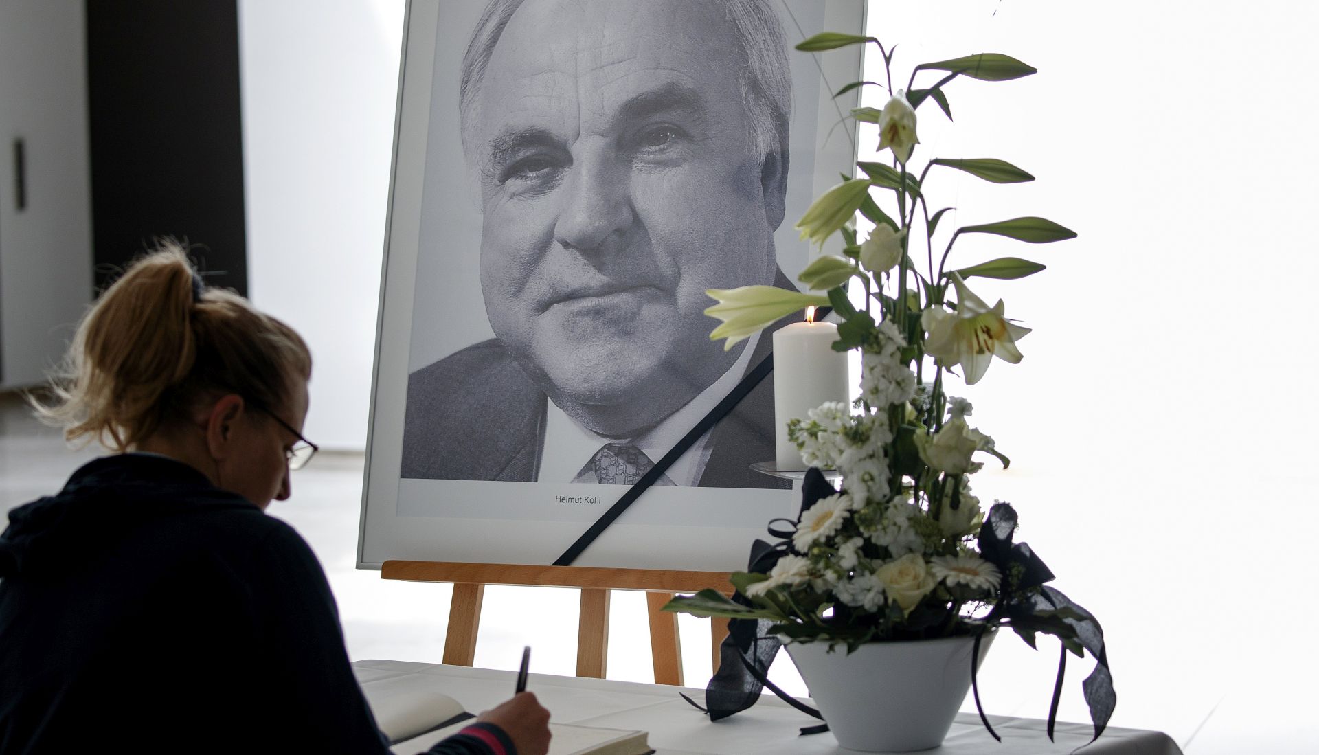 epa06032832 A woman writes in a book of condolence in front of a portrait photo of former Chancellor Helmut Kohl in Berlin, Germany, 16 June 2017. Kohl was the sixth Federal Chancellor of the Federal Republic of Germany from 1982 to 1998. Kohl has died at the age of 87 in his home in Ludwigshafen, on 16 June 2017.  EPA/CARSTEN KOALL