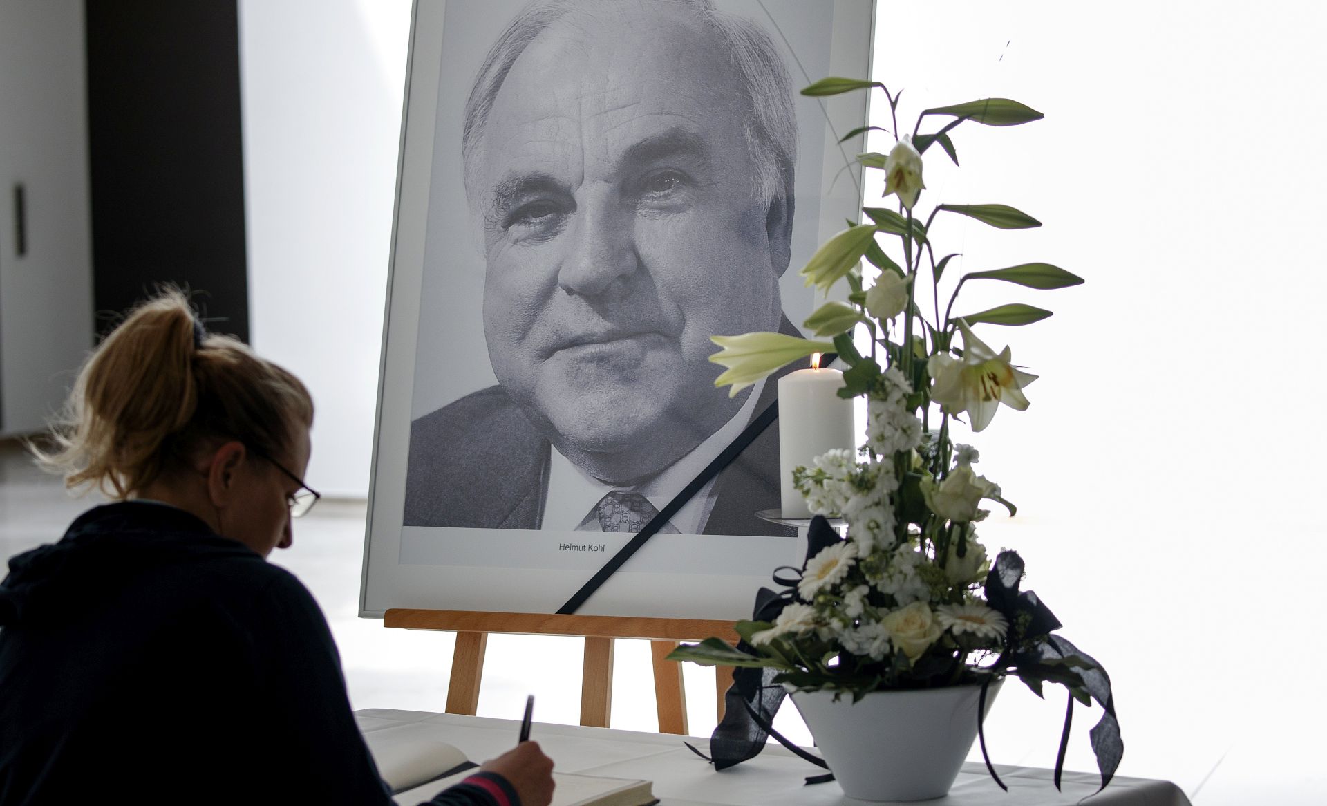 epa06032832 A woman writes in a book of condolence in front of a portrait photo of former Chancellor Helmut Kohl in Berlin, Germany, 16 June 2017. Kohl was the sixth Federal Chancellor of the Federal Republic of Germany from 1982 to 1998. Kohl has died at the age of 87 in his home in Ludwigshafen, on 16 June 2017.  EPA/CARSTEN KOALL