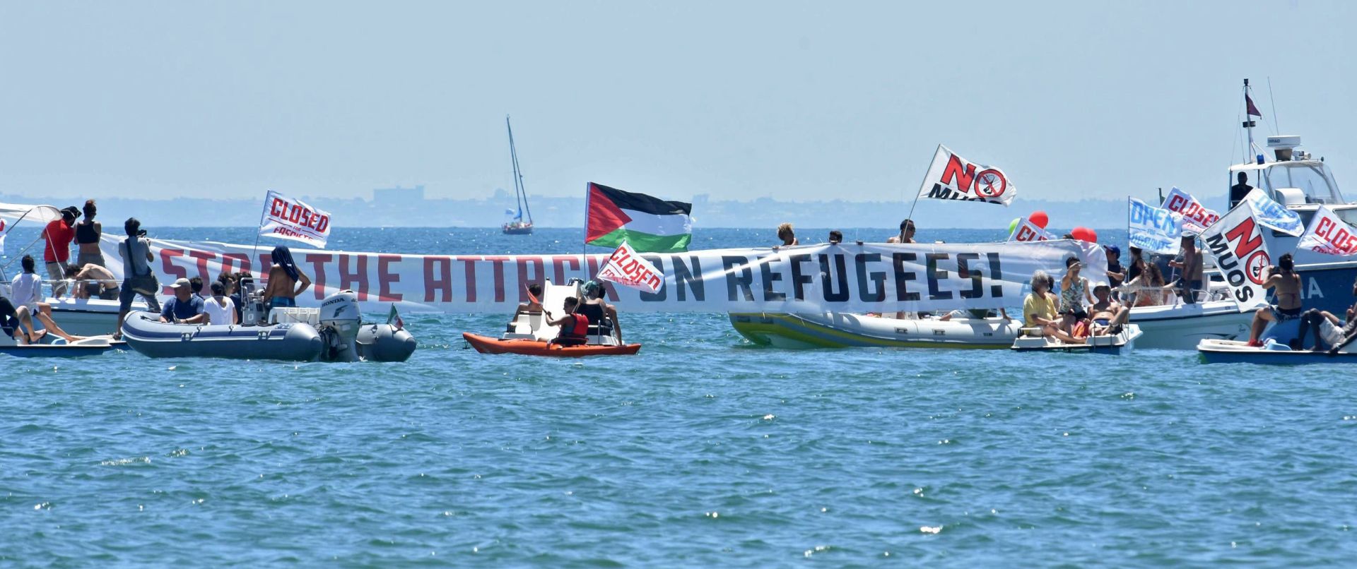 epa06116019 People take part in the event 'City Flotilla, at Sea Against Racism' in Catania, Sicily Island, Italy, 29 July 2017. Canoes, pedal boats and boats of all kinds are mobilized to block the eventual entry into the port of Catania of the C-Star ship from Generation Identity, which aims to disrupt migrant rescues in the Mediterranean Sea.  EPA/Orietta Scardino