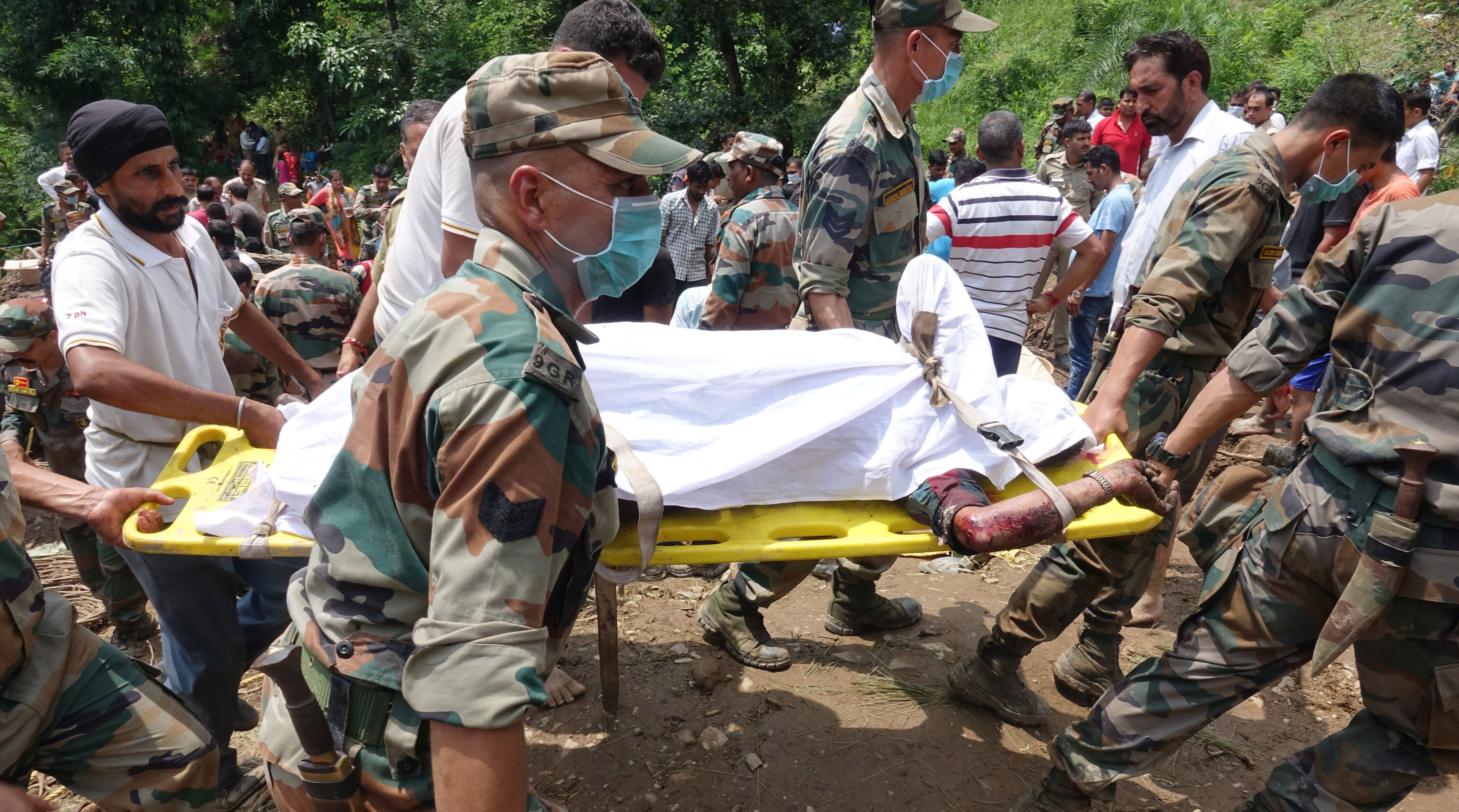 epa06141783 Members of the Indian Army and rescue teams carry the body of a victim at the site of a landslide in Mandi, Himachal Pradesh, India, 13 August 2017. At least seven people were killed and over 20 went missing after a massive landslide swept away buses near the Mandi-Pathankot national highway, media reported.  EPA/SANJAY BAID