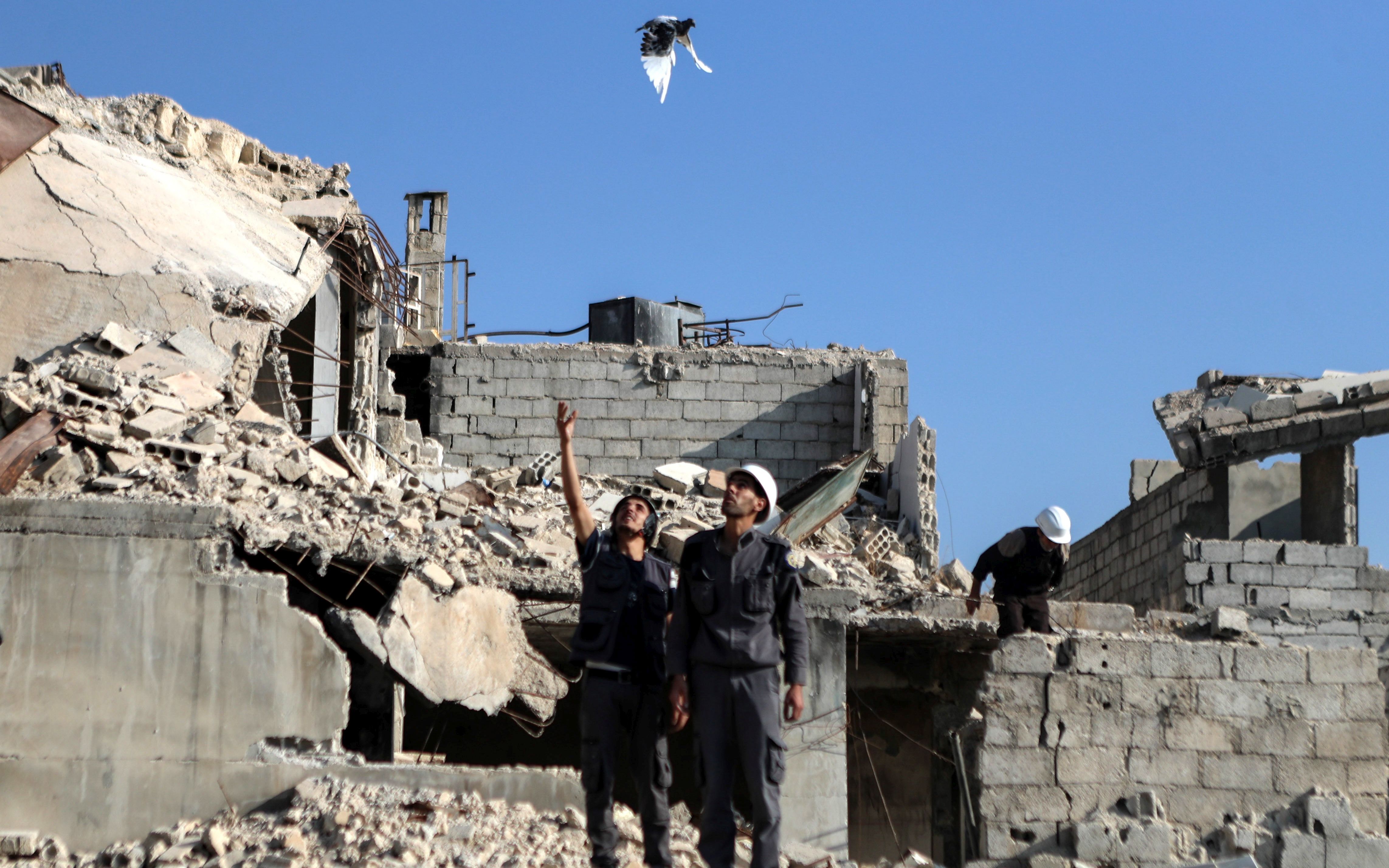 epa06156438 A volunteer let go of a pigeon as a symbol of peace to the world according to Serag Mahmood, the offical speaker of the White Helmets in Rural Damascus during a soliderity protest among the rubbles of destroyed houses, Zamalka, rebel-held eastern al-Ghouta, Syria, 22 August 2017. The protest was in the memory of the chemical attack on Eatsern al-Ghouta in 21 August 2013 that killed unconfirmed number of people that range between 281 to 1729 according to various sources.  EPA/MOHAMMED BADRA