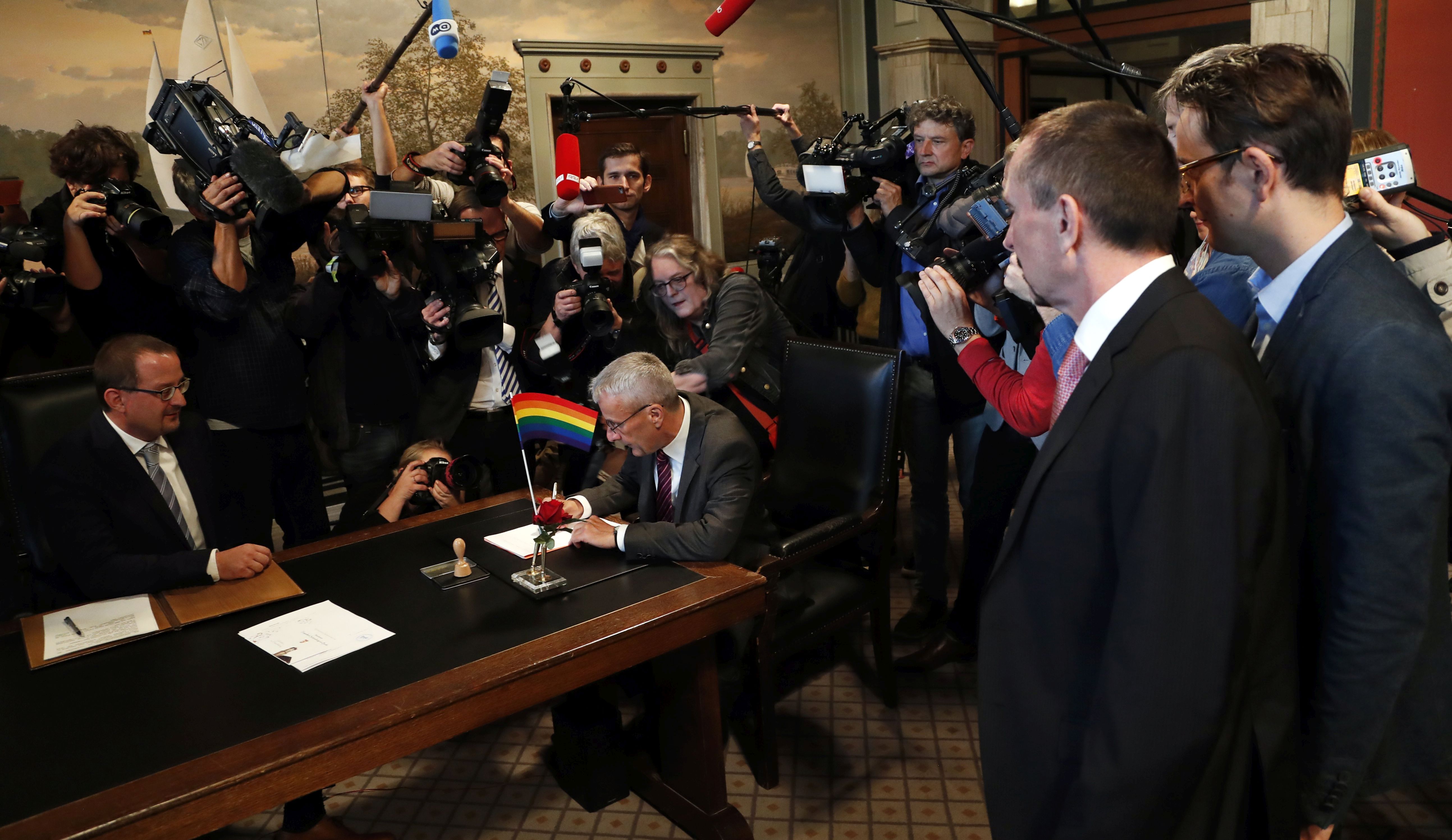 epa06237336 Karl Kreile (2-R) looks his partner Bodo Mende as he signs the marriage certificate during the first civil wedding ceremony between two men in Berlin, Germany, 01 October 2017. The same sex marriage law that was approved by the German Parliament in June becomes effective from the 01 October 2017. Till now gay and lesbian couples could only register partnerships, the same sex marriage law allow them to adopt children and equals their rights to those of heterosexual couples.  EPA/FELIPE TRUEBA