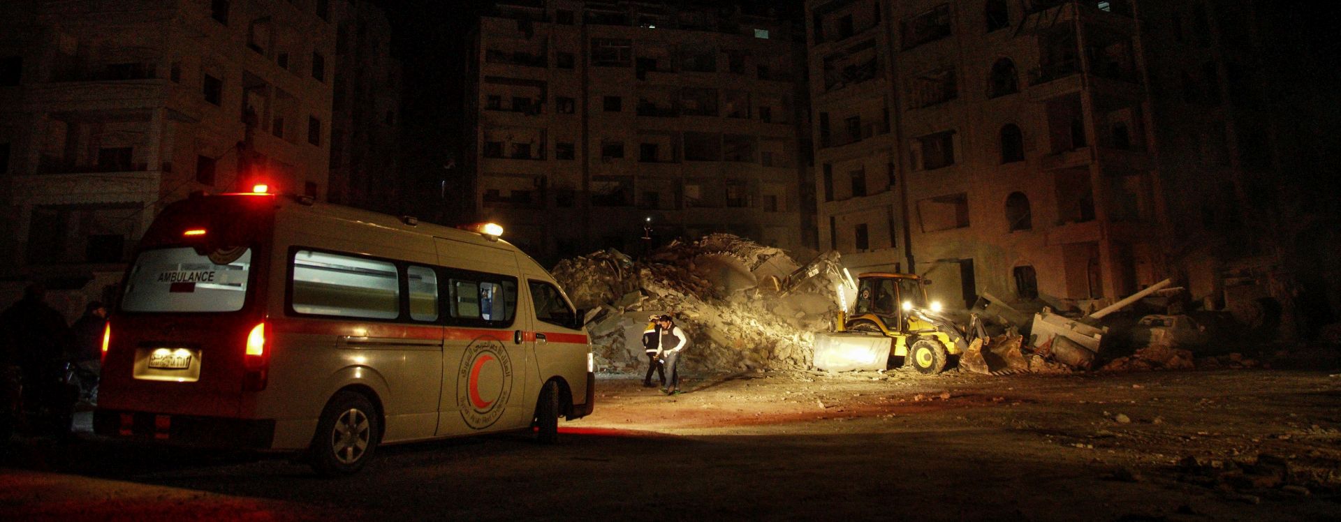 epa06496993 Syrian Arab Red Crescent (SARC) volunteers walk next to an ambulance near civilian buildings which were destroyed in airstrikes in Idlib City, Syria, 04 February 2018. The number of killed and wounded is unclear. According to activists the airstrikes were conducted by Russian warplanes.  EPA/YAHYA NEMAH
