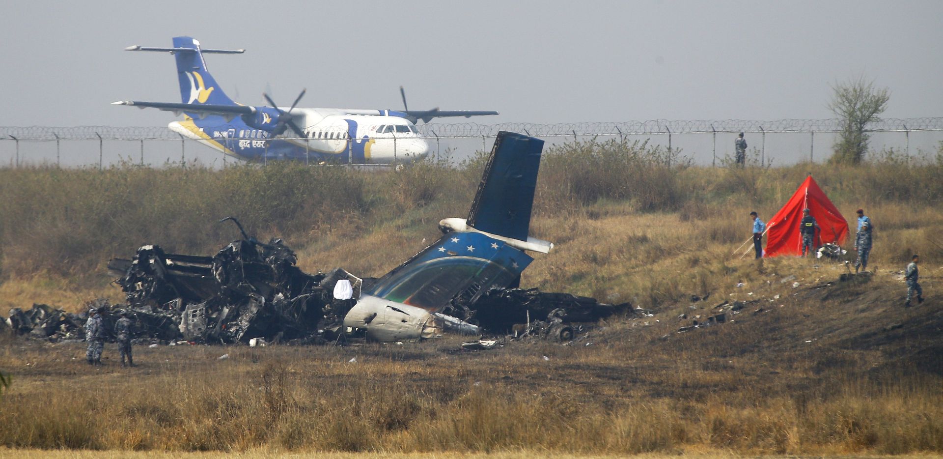 epa06599791 Nepalese police officers inspect the site of the crash next to the wreckage of US-Bengla flight BS211 at the Tribhuvan International Airport in  Kathmanduu, Nepal, 13 March 2018. Bangladeshi US-Bengla plane had crashed on 12 March while landing at the airport with 71 passengers and crew onboard. According to reports 49 people have died and 22 survived. The cause of the crash is yet unknown.  EPA/NARENDRA  SHRESTHA