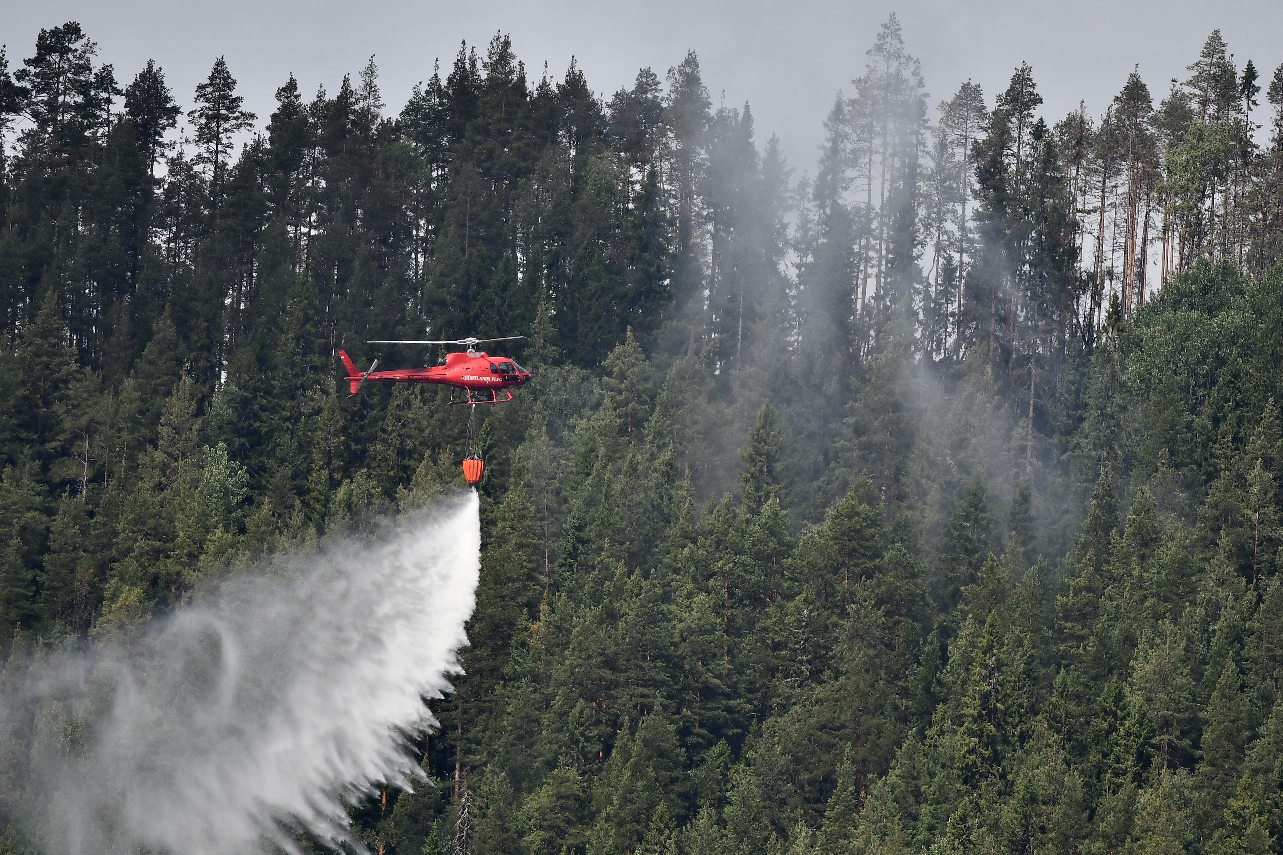 epa06903955 A chartered helicopter dumps a load of water ontio a smouldering spot in a forest near the village Grotingen in the Bracke municipality to fight one of many wild fires in central Sweden, 22 July 2018. Sweden meanwhile has called for emergency assistance from the European Union to tackle the dozens of wildfires raging across the country. Italian and French fire fighting planes as well as fire engines from Poland and firefighters from other EU countries joined in the efforts to contain and extinguish the wild fires.  EPA/ROBERT HENRIKSSON SWEDEN OUT