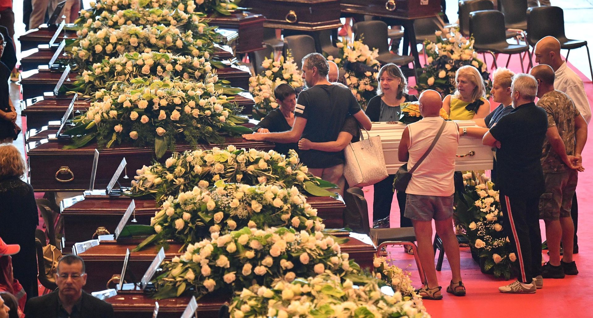epa06955378 People pay their respects as victims of the Morandi bridge disaster lie in coffins at the Fiera di Genova exhibition centre prior to the State funeral, in Genoa, Italy, 18 August 2018. The Morandi bridge partially collapsed on 14 August, killing at least 41 people.  EPA/LUCA ZENNARO