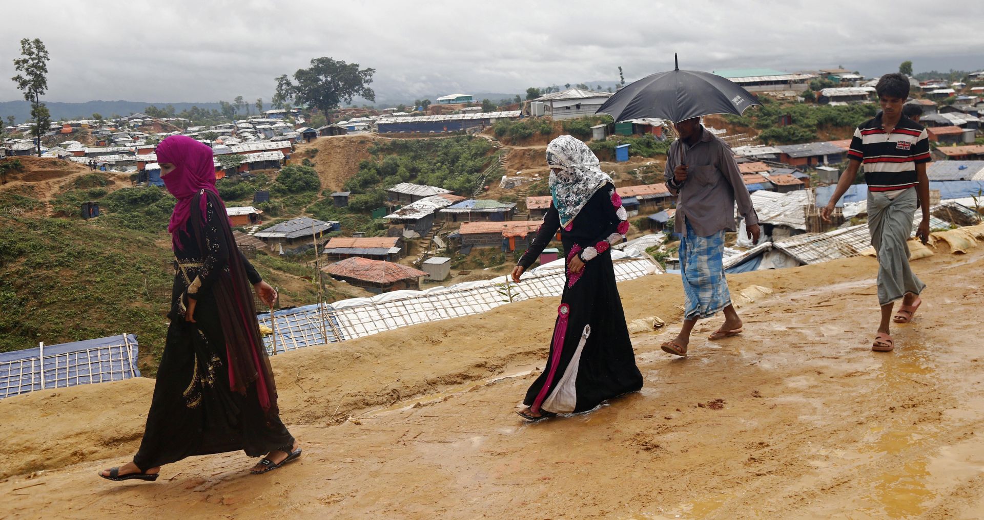 epa06973586 Rohingya refugees during the rain season walk on a muddy road along a makeshift camp in Kutubpalang, Cox Bazar district, Bangladesh, 26 August 2018. The day before marked the first anniversary of neighboring Myanmar's launch of military operation in the Rakhine State in response to attacks by the Arakan Rohingya Salvation Army on police posts. Security forces and their proxies are believed to have killed thousands of Rohingyas, burned villages to the ground, committing widespread sexual violence and droving more than 700,000 people to flee the country across the border to Bangladesh.  EPA/MONIRUL ALAM