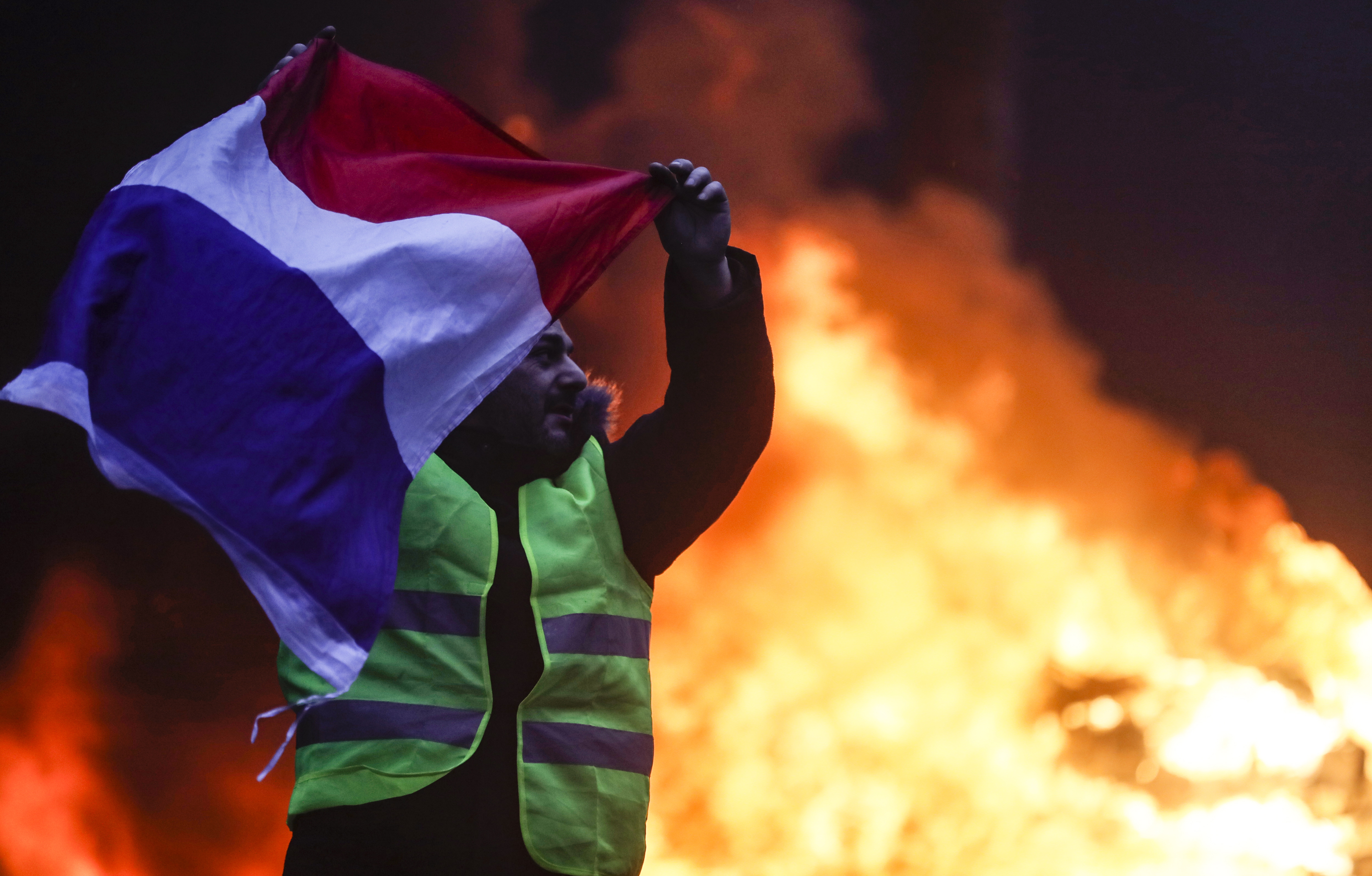 epa07201679 Cars burn, while protesters wearing yellow vests (gilets jaunes) clash with riot police near the Arc de Triomphe as part of a demonstration over high fuel prices on the Champs Elysee in Paris, France, 01 December 2018. The so-called 'gilets jaunes' (yellow vests) are a protest movement, which reportedly has no political affiliation, is protesting across the nation over high fuel prices.  EPA/ETIENNE LAURENT