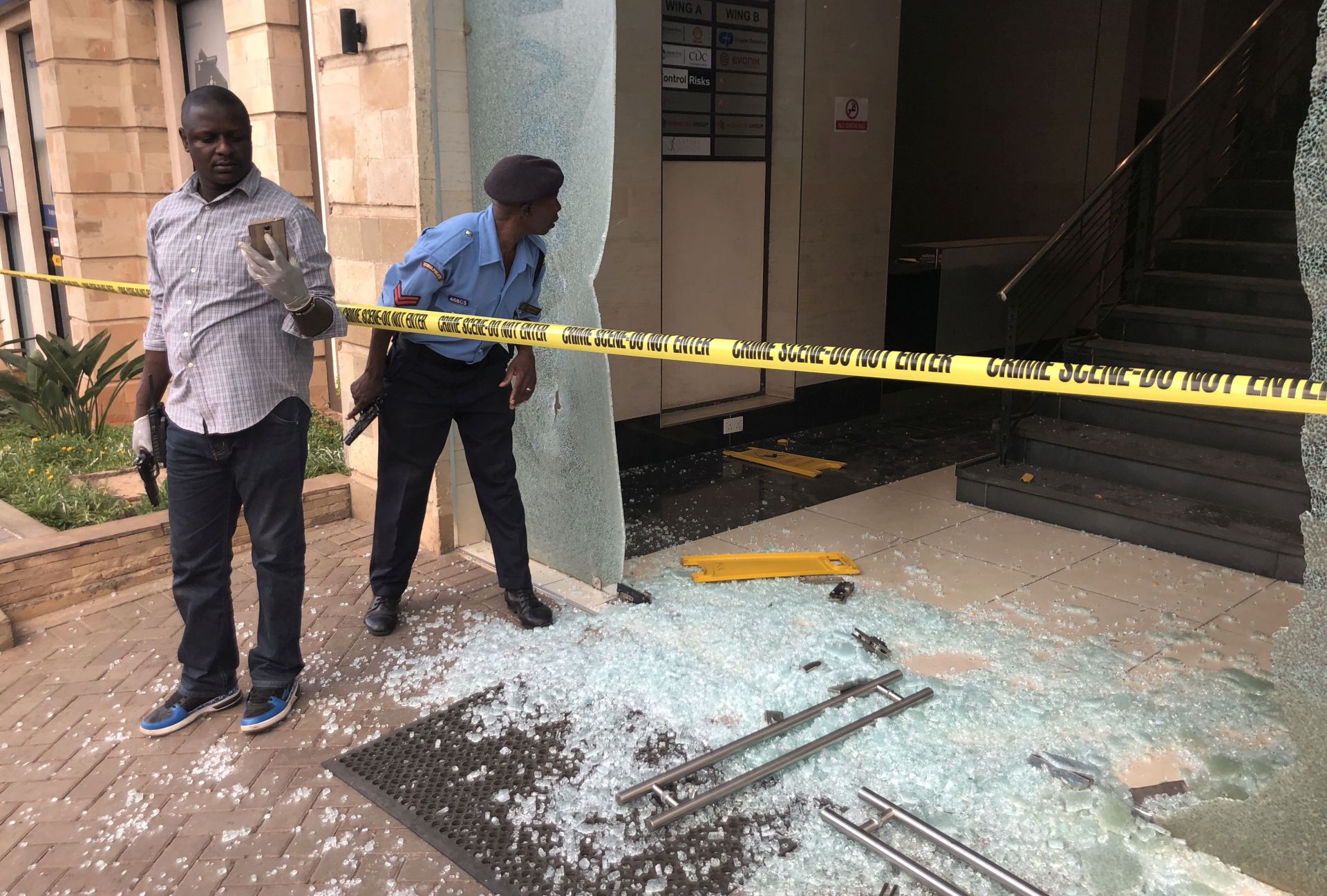 epa07286595 Armed plain clothes officials secure the damaged entrance of an hotel during an ongoing gunfire and explosions in Nairobi, Kenya, 15 January 2019. According to reports, a large explosion and sustained gunfire sent workers fleeing for their lives at an upscale hotel and office complex in the Kenyan capital of Nairobi.  EPA/DAI KUROKAWA