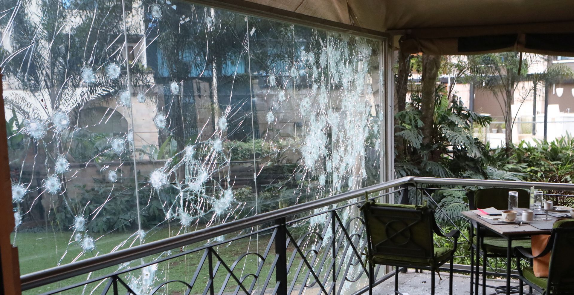epa07287089 A motionless body (R), of a victim is seen lying on a table next to a bullet holes riddled glass (L), at a restuarant is seen during an ongoing gunfire and explosions in Nairobi, Kenya, 15 January 2019. According to reports, a large explosion and sustained gunfire sent workers fleeing for their lives at an upscale hotel and office complex in the Kenyan capital of Nairobi.  EPA/DANIEL IRUNGU EDITORS IMAGE CONTAINS GRAPHIC CONTENT
