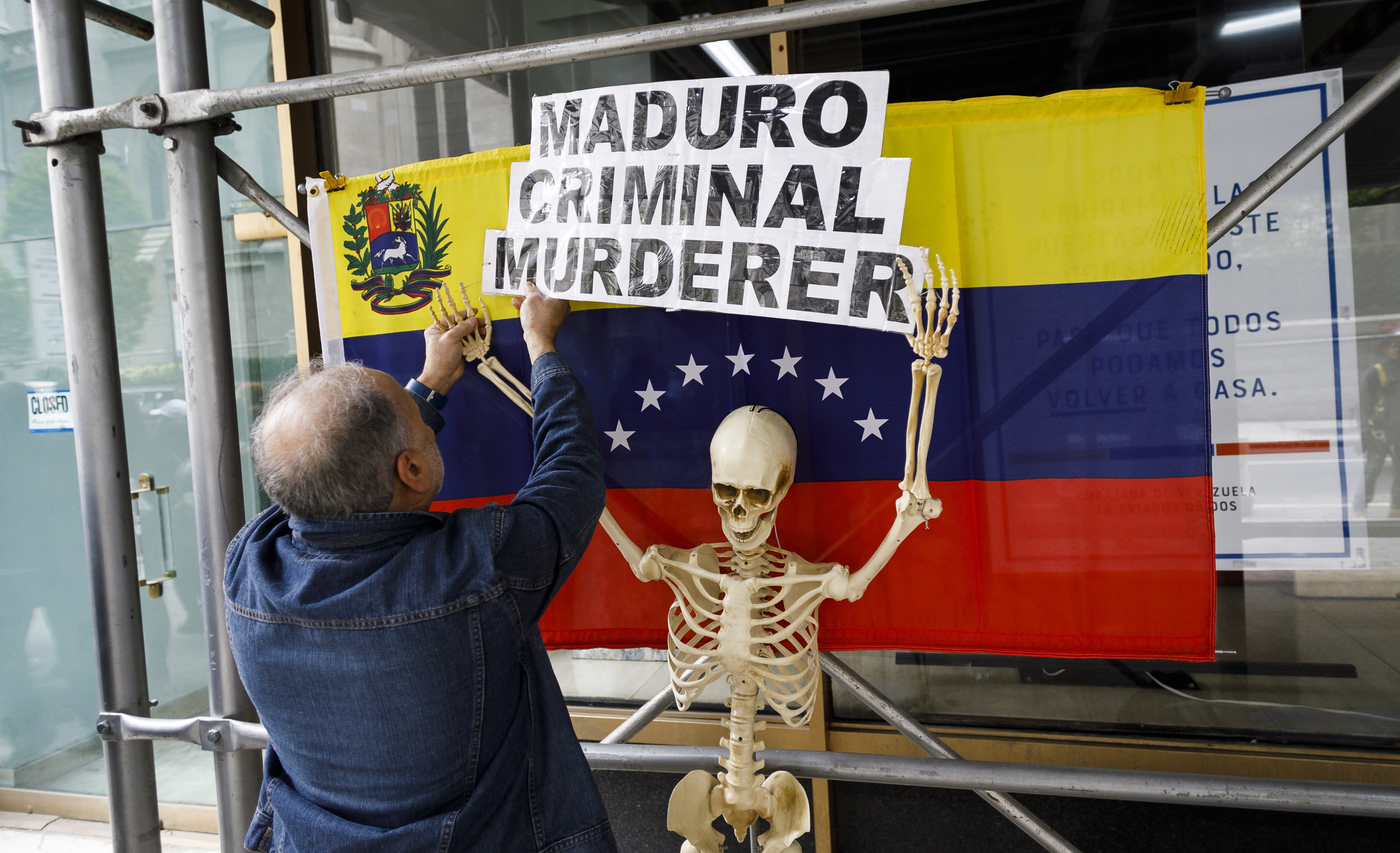 epa07538871 A supporter of Venezuela opposition leader Juan Guaido hangs a sign during a rally in front of the now-shuttered Venezuelan consulate in New York, New York, USA, 30 April 2019.The struggle for power in Venezuela between Guaido, who declared himself the interim president of Venezuela earlier this year, and President Nicolas Maduro escalated this week and there is speculation that the country's military may been shifting its allegiance to Guaido's opposition party.  EPA/JUSTIN LANE