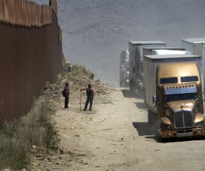 epa07626208 Two men who are fixing the road in exchange for tips watch as trucks drive along a dirt road next to the U.S.-Mexico border fence toward the commercial border inspection stationn in Tijuana, Mexico, on 04 June 2019, following US President Donald J. Trump's decision to impose tariffs on Mexico. The truck will queue in line with several hundred other trucks waiting to cross the border into San Diego, California, USA. US President Donald J. Trump stated he is planning to implement his decision to impose five percent tariffs on goods imported into the US from Mexico, with a five percent increase each month until October, if Mexican officials do not stop undocumented migrants from crossing into the US from the two nation's shared border.  EPA/David Maung