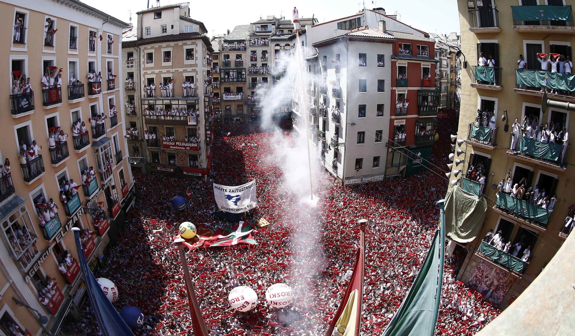 epa07698560 People attend the traditional firing of the 'chupinazo' that marks the beginning of the Festival of San Fermin 2019 at the City Hall Square in Pamplona, Spain, 06 July 2019. The firing of a rocket, the chupinazo, from the City Hall's balcony at midday signals the beginning of event. The festival, locally known as Sanfermines, is held annually from 06 to 14 July in commemoration of the city's patron saint. Hundreds of thousands of visitors from all over the world attend the fiesta. Many of them physically participate in the highlight event - the running of the bulls, or encierro - where they attempt to outrun the bulls along a route through the narrow streets of the old city.  EPA/JESUS DIGES / POOL