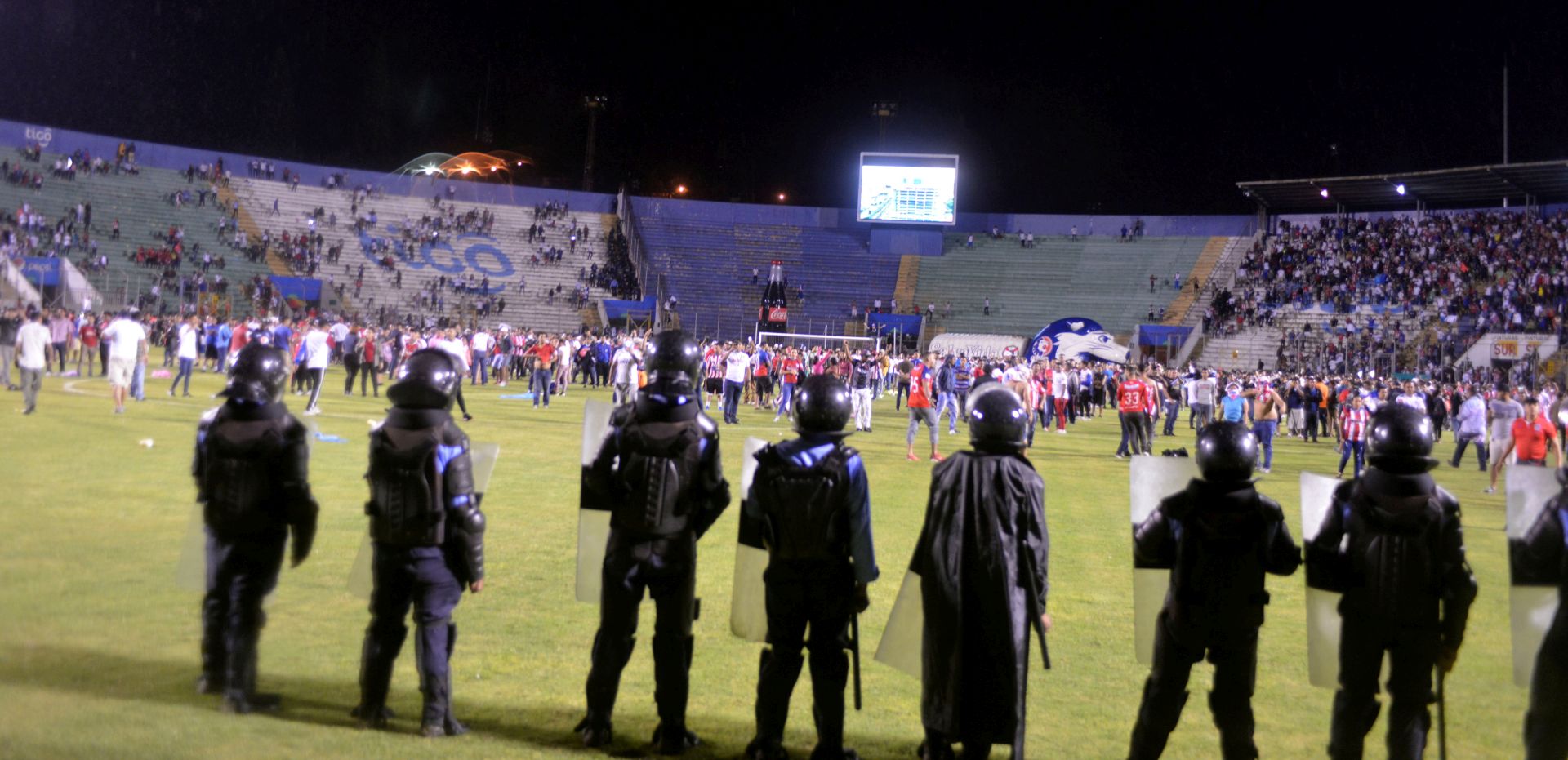 epa07778805 Supporters enter the field and protect themselves from tear gas released by authorities, due to riots outside the National Stadium, due to cancellation of the classic soccer match between teams Olimpia and Motagua in Tegucigalpa, Honduras, 17 August 2019. At least three players, including Paraguayan Roberto Moreira and Argentine Jonathan Rougier, were slightly injured on Saturday in an attack on the bus of the Honduran team Motagua before the match corresponding to the fifth day of the AperturaTournament.  EPA/STR