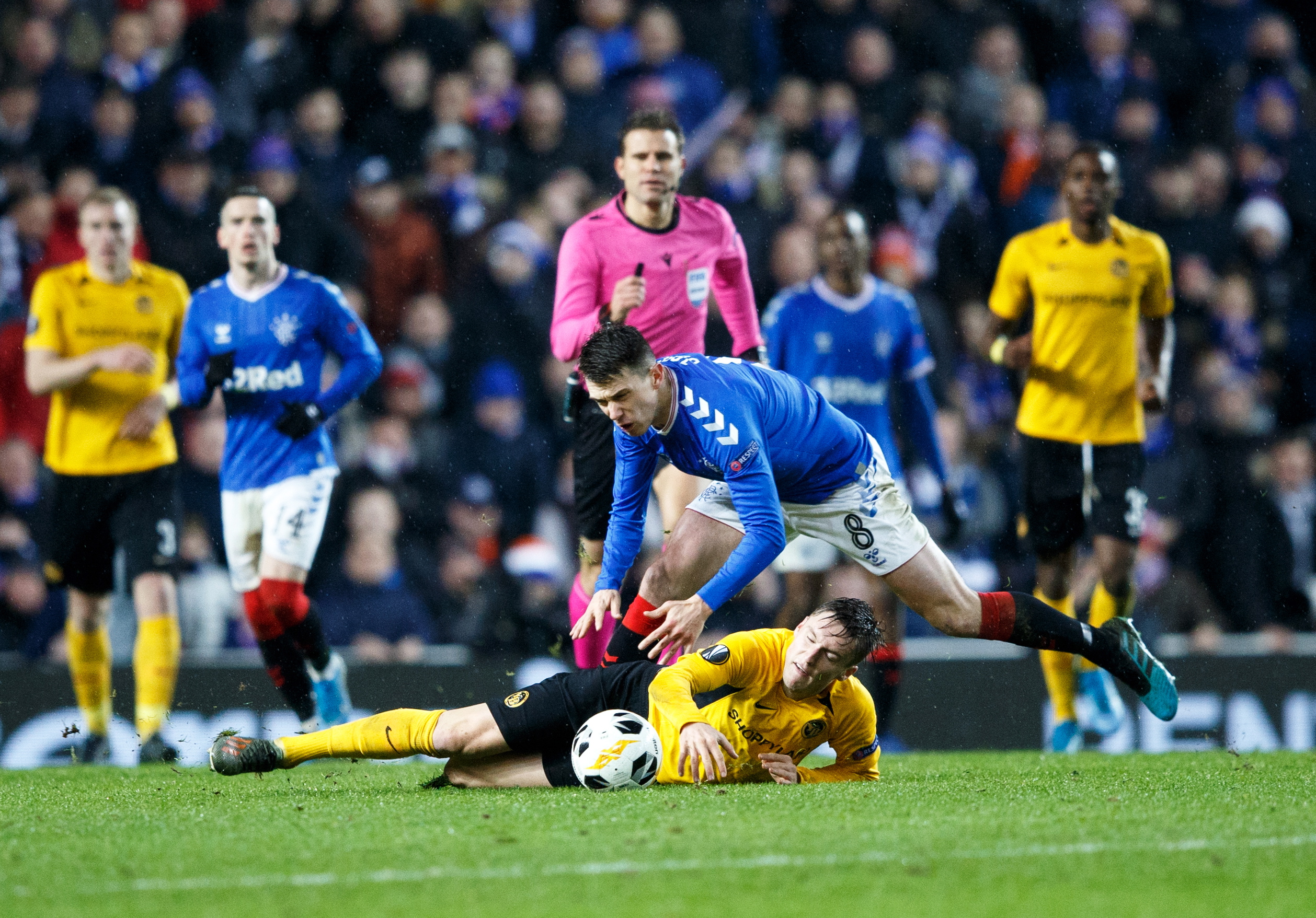 epa08067121 Referee Felix Brych (C) gives a yellow card to Ryan Jack (L) of Rangers after this challenge on Young Boys' Michel Aebischer (ground)  during the UEFA Europa League match Rangers v BSC Young Boys in Glasgow, Britain, 12 December 2019.  EPA/ROBERT PERRY