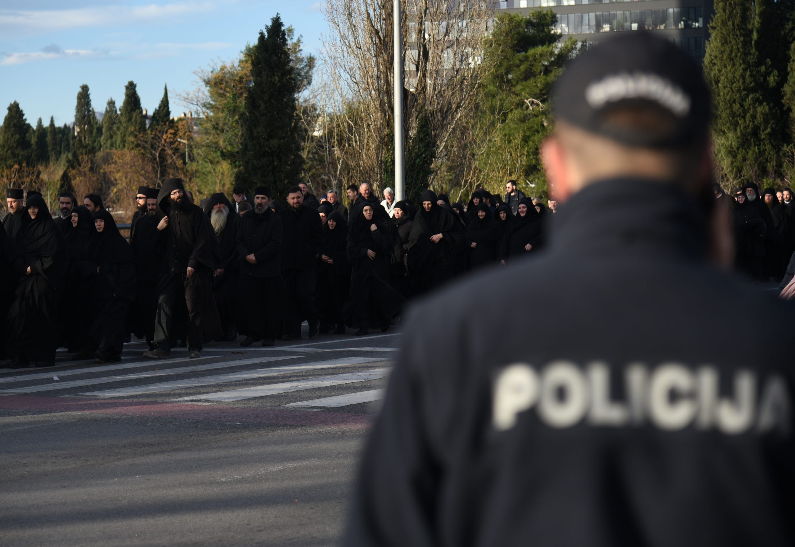 epa08088794 A police officer keeps watch as Serbian Orthodox Church priests and nuns in Montenegro take part in a protest rally in Podgorica, Montenegro, 24 December 2019. The Serbian Orthodox Church in Montenegro is protesting against a controversial new law on religion, which the church has called a plot to rob it of its property. Montenegro's government proposed a new bill on religion requiring all religious communities, including Catholic and Orthodox churches, to register their immovable assets as state property. The law also states that religious communities can only retain their assets if they can produce evidence of the right to ownership, triggering allegations from the Serbian Church that the government plans to dispute its holdings.  EPA/BORIS PEJOVIC