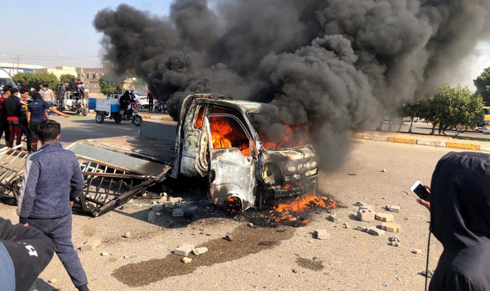 epa08104221 Iraqi protesters gather as smoke rises from a burning truck after clashes between protesters and unknown armed group in Nasiriyah city, some 370km southeast of Baghdad, Iraq, 05 January 2020. One protester was killed and dozens others were wounded when unknown gunmen attacked the site of protests in Nasiriyah city following their attempt to hold a symbolic funeral procession for the Iraqi militia commander Abu Mahdi al-Muhandis and Qasem Soleimani, the head of Iran's Islamic Revolutionary Guard Corps' elite Quds Force inside the protest location, a security source said.  EPA/STR