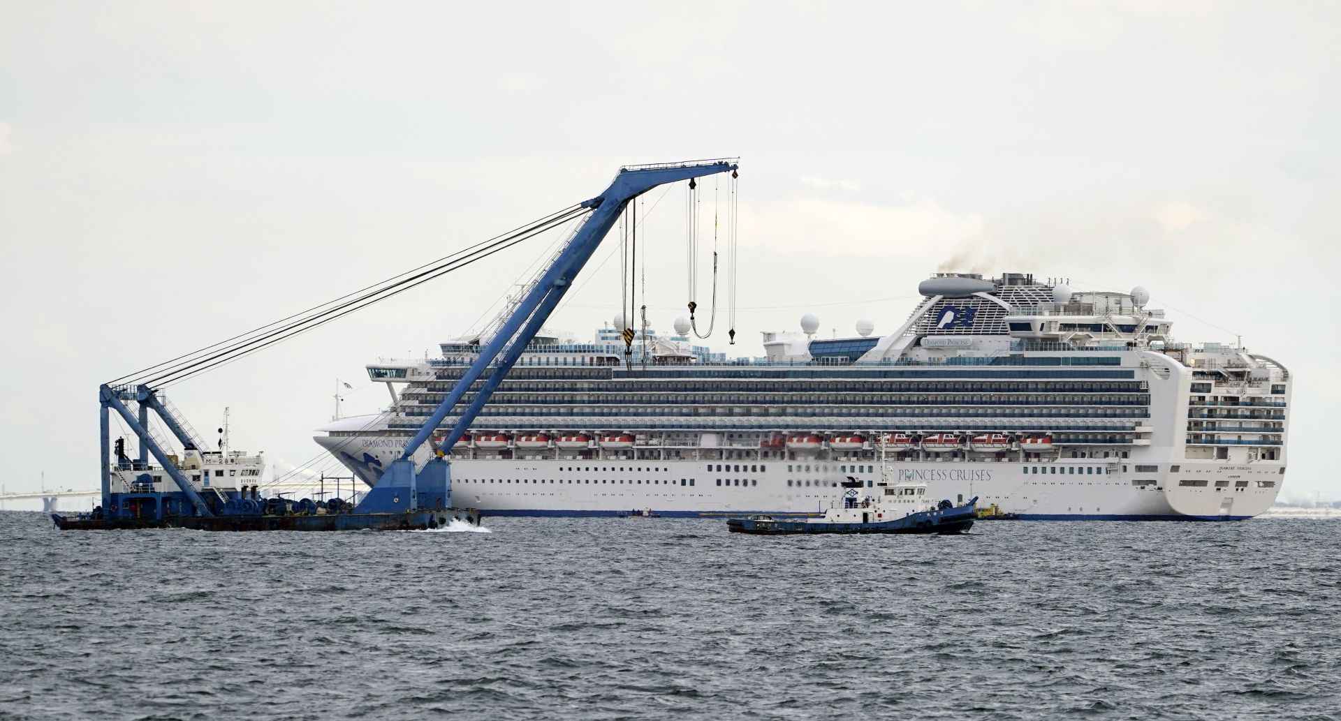 epa08191509 A large crane is pulled past the Diamond Princess cruise ship, anchored in quarantine off the port of Yokohama, in Yokohama, Japan, 04 February 2020. More 3,700 people, including passengers and staff members, are being tested for coronavirus infection after a passenger who was previously onboard tested positive for the virus in Hong Kong on 01 February.  EPA/FRANCK ROBICHON