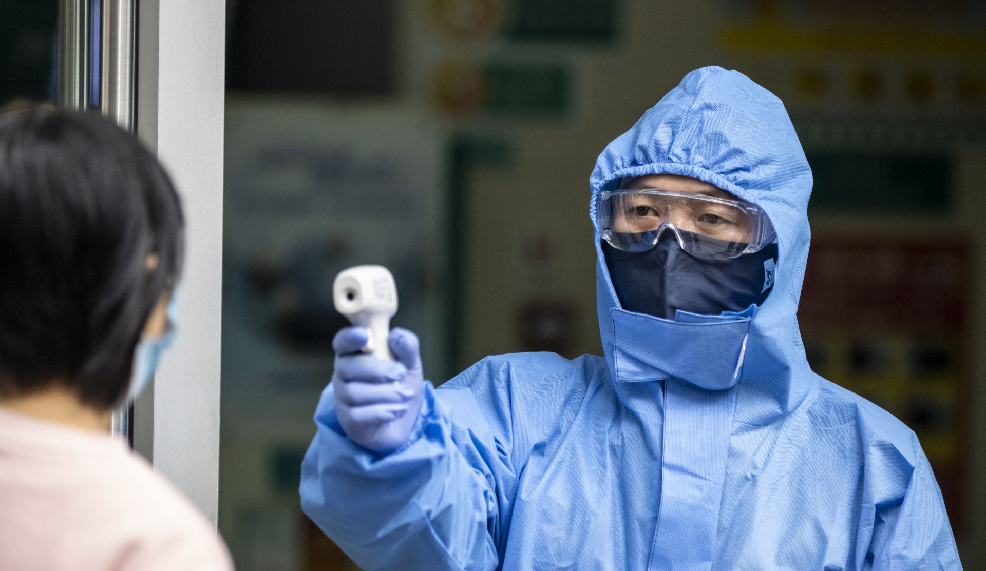 epa08243115 A security guard wearing a mask and protective gear measures visitors' body temperature at the entrance to a bank in Guangzhou, Guangdong province, China, 24 February 2020. The outbreak of Covid-19 coronavirus, which originated in the Chinese city of Wuhan, has so far killed at least 2,626 people and infected 79,702 others worldwide, mostly in China.  EPA/ALEX PLAVEVSKI
