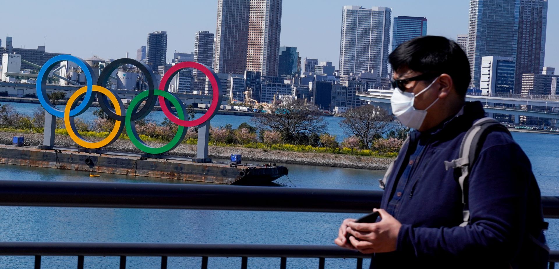 epa08273707 A tourist wearing a mask is seen near the Olympic rings in Tokyo, Japan, 06 March 2020. According to Japan's Olympic Minister, the Coronavirus outbreak has forced several major events to be cancelled in Japan, which could see the 2020 Summer Olympic Games postponed until later in the year.  EPA/CHRISTOPHER JUE
